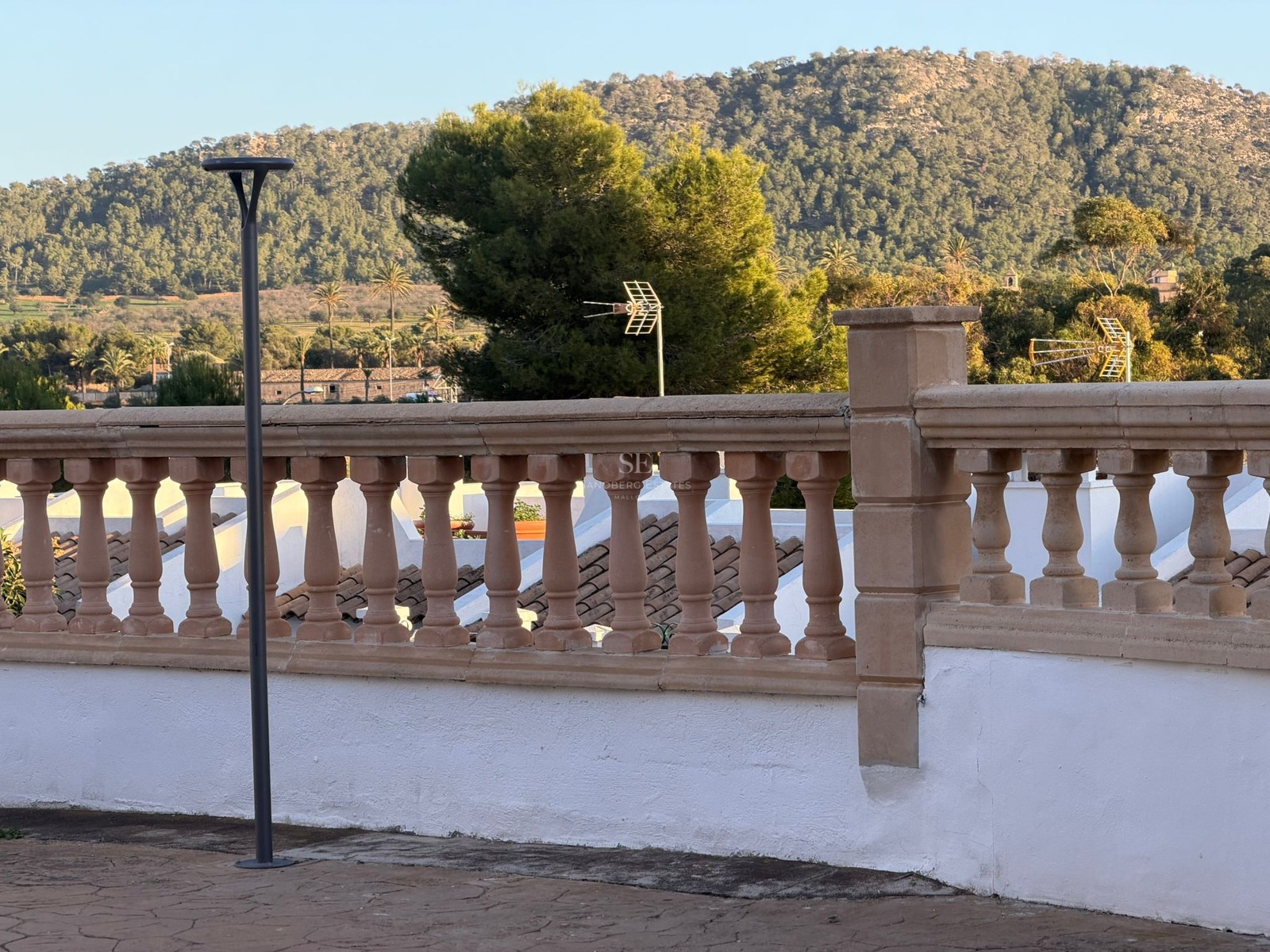 A stone balustrade on a white terrace overlooking a lush green mountain under a clear sky.