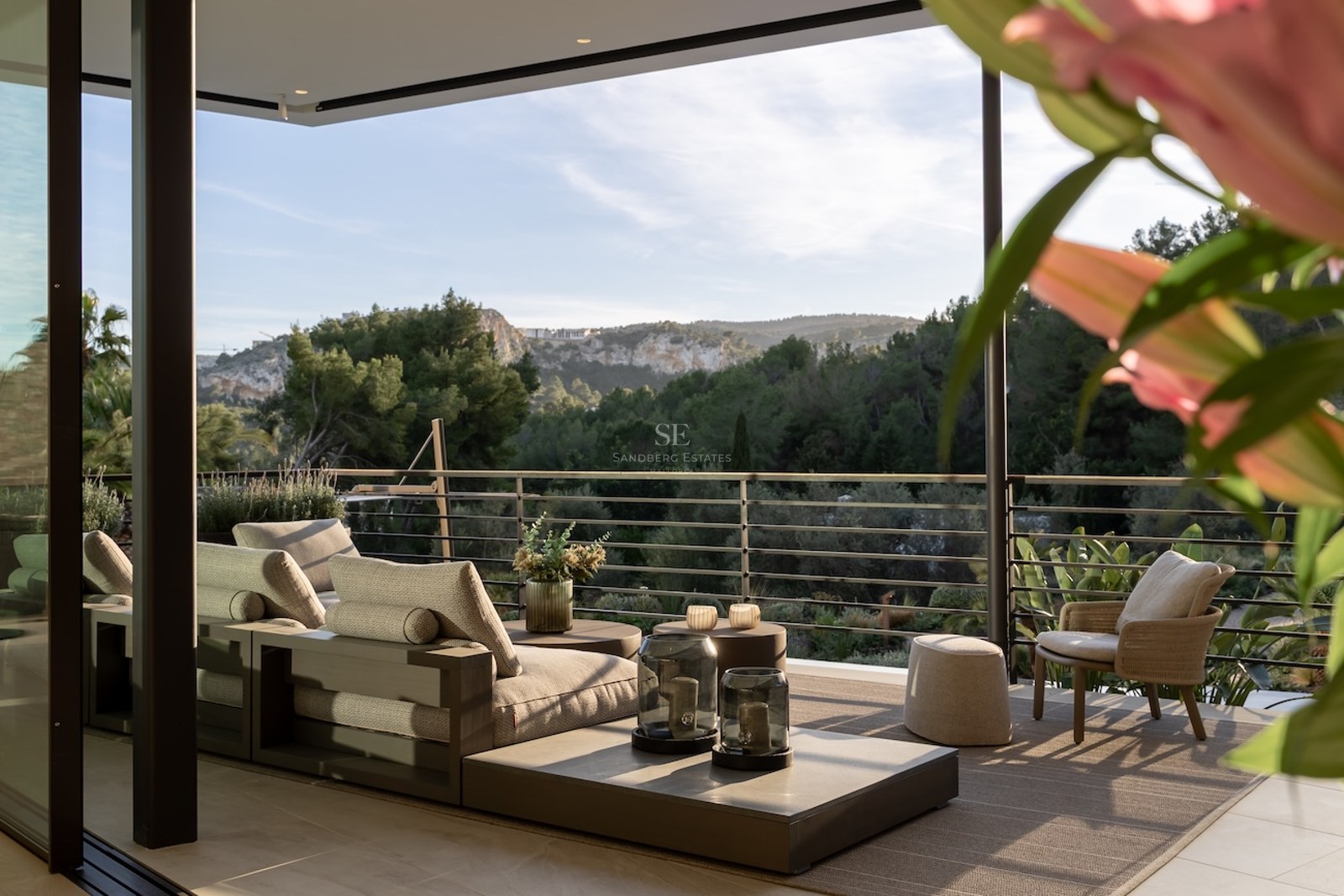 Terraza moderna con sofás modulares de madera con vistas a un valle verde y colinas arboladas bajo un cielo despejado.