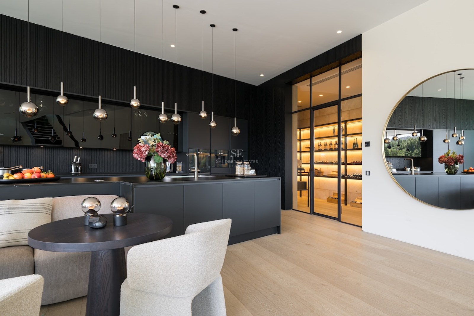 Cocina moderna en negro mate con una isla grande y una bodega de vino con paredes de cristal al fondo.