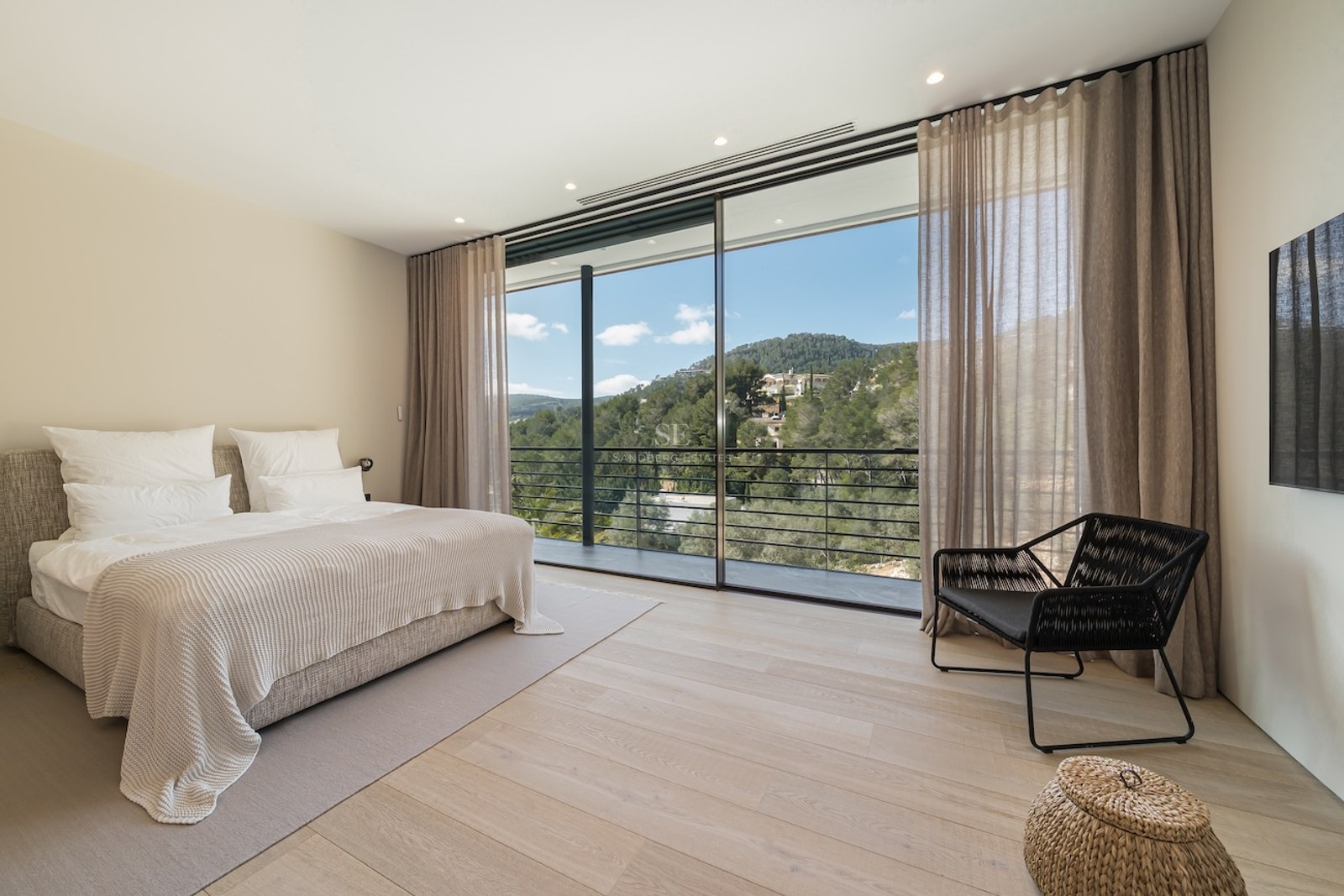 Dormitorio moderno con suelos de madera clara, grandes ventanales de suelo a techo y vistas a colinas verdes.