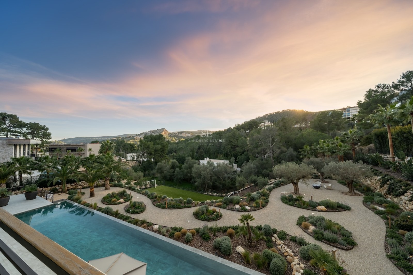 Vue en hauteur d'une piscine à débordement turquoise bordant un jardin méditerranéen paysager au crépuscule.