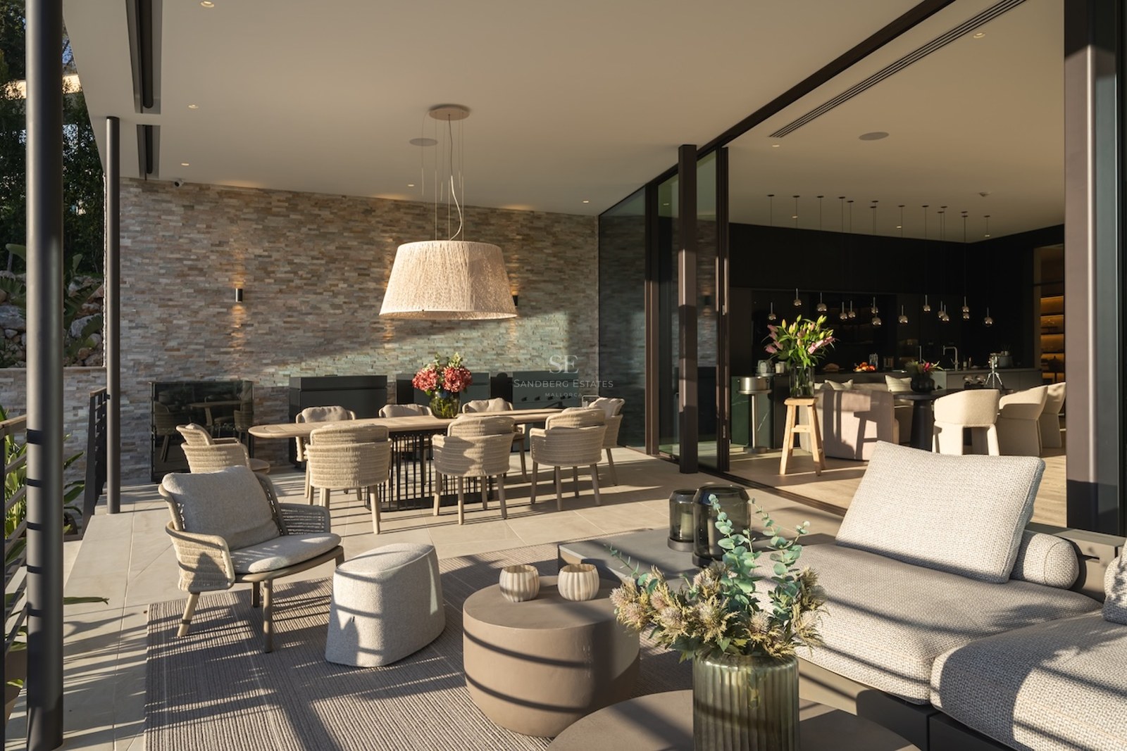 Terraza cubierta de lujo con pared de piedra natural, comedor exterior y zona lounge conectada al interior.
