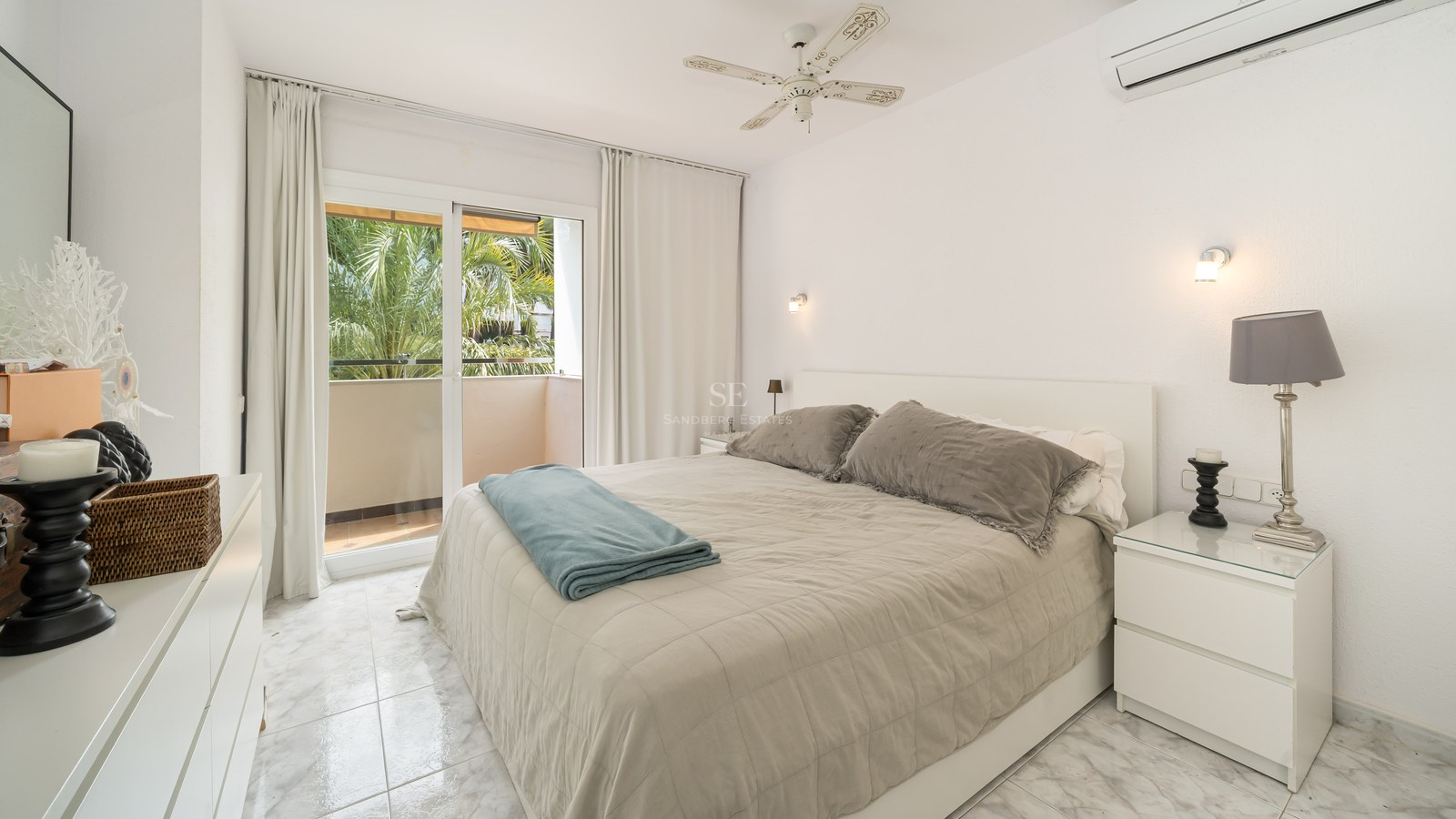 Chambre lumineuse avec lit double, sol en marbre et balcon offrant une vue sur des palmiers.