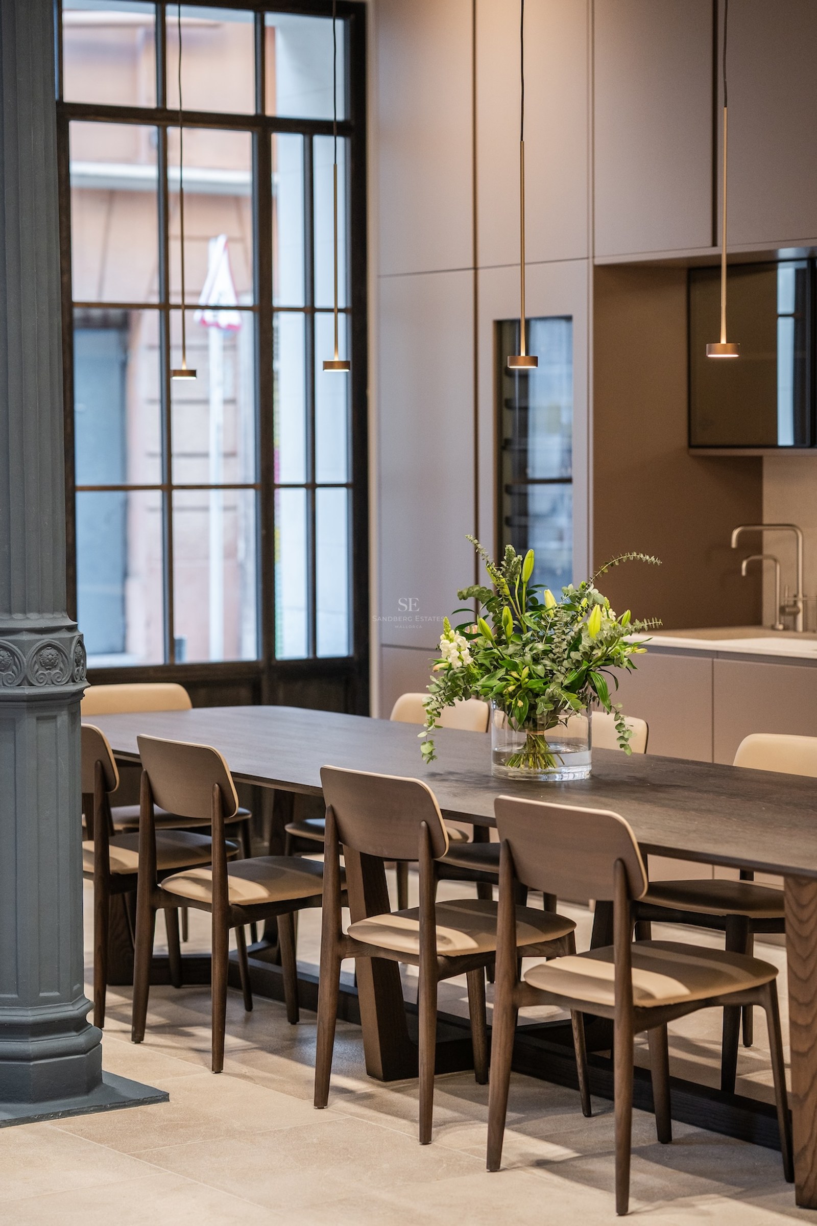 Mesa de comedor de madera oscura con sillas modernas, lámparas colgantes minimalistas y una columna decorativa.