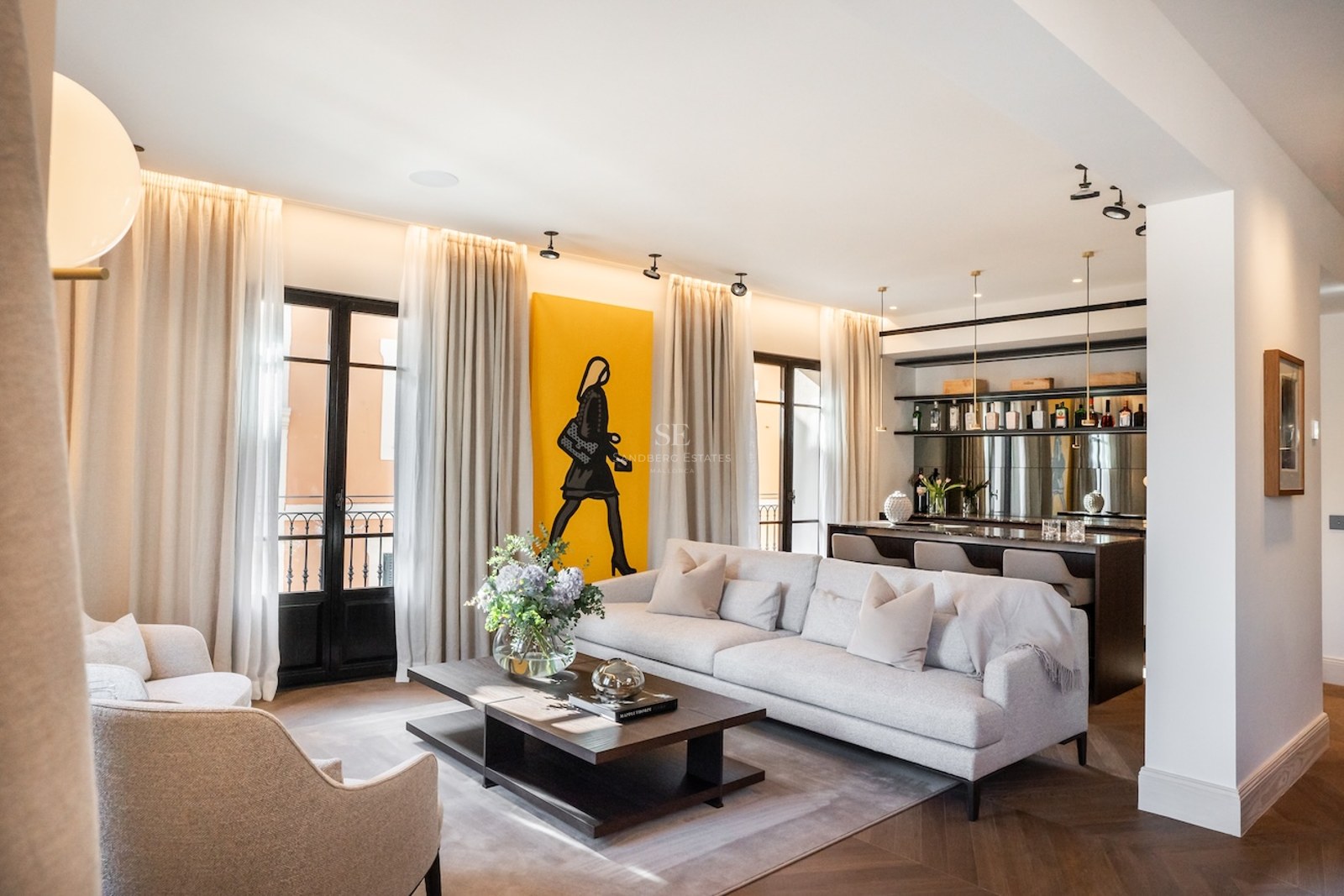 Sala de estar moderna con sofá gris, suelo de espiga, un gran cuadro amarillo y una zona de bar.