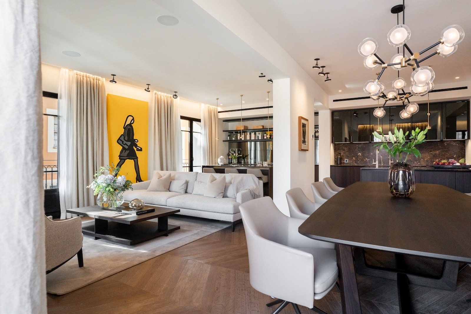 Salón de planta abierta con sofá gris, arte amarillo en la pared y zona de comedor con lámpara de diseño.