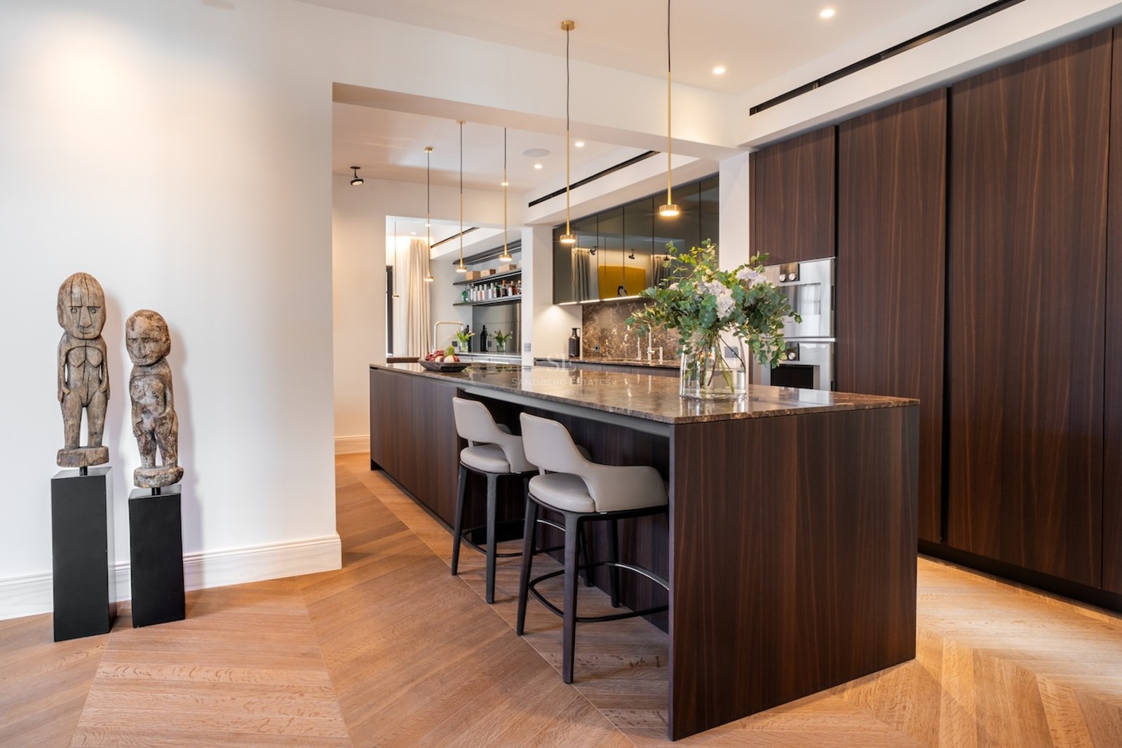 Cocina contemporánea con isla de madera oscura, encimera de mármol, taburetes de cuero y suelo de madera en espiga.