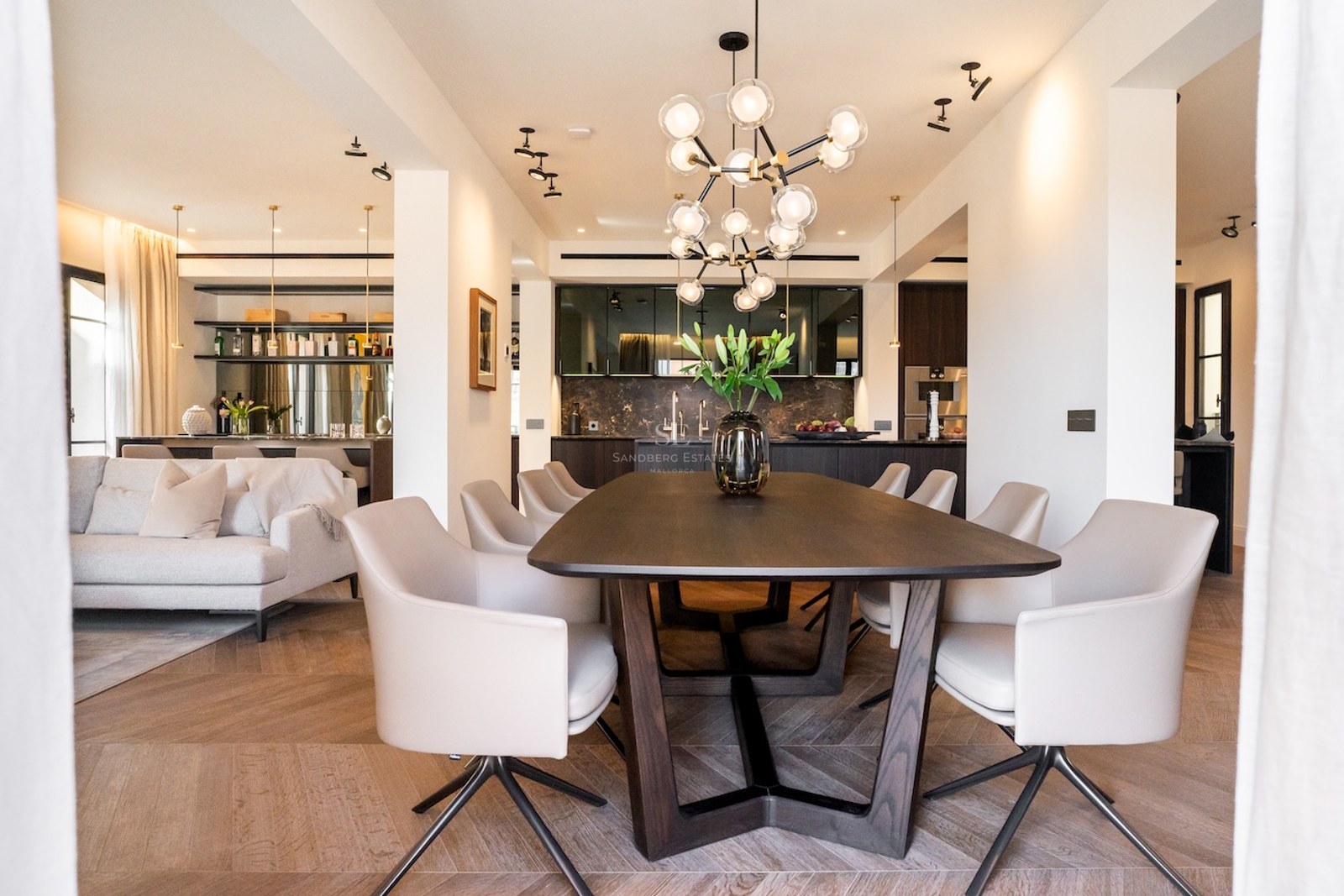 Comedor moderno con mesa de madera oscura, sillas blancas y lámpara de esferas en una casa de lujo.
