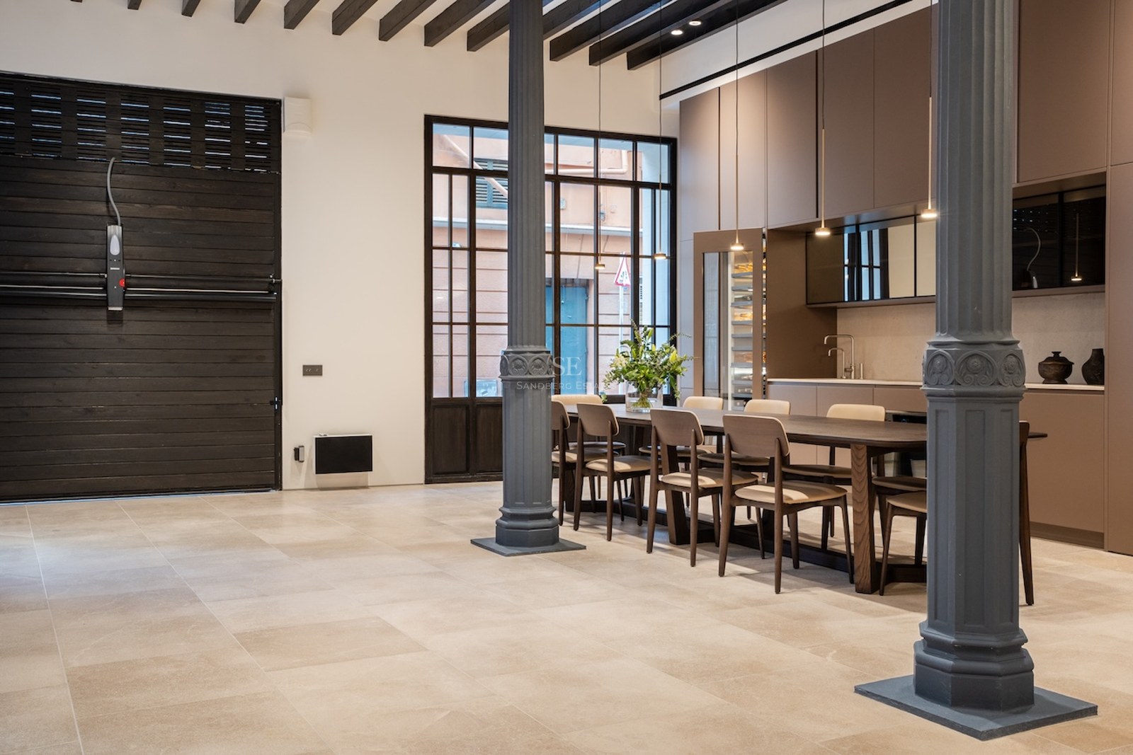 Comedor industrial con columnas estriadas, mesa de madera larga y vigas vistas en un espacio abierto.