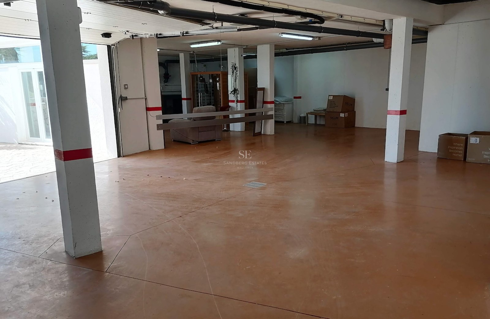 Interior view of a large private underground garage with terracotta-toned floors, white pillars, and overhead lighting.