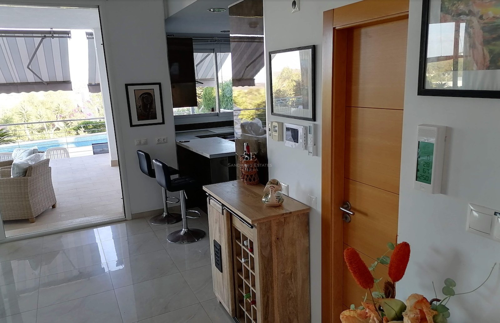 Interior view showing a modern living area with wine cabinet, leading to a sun-drenched terrace and swimming pool.