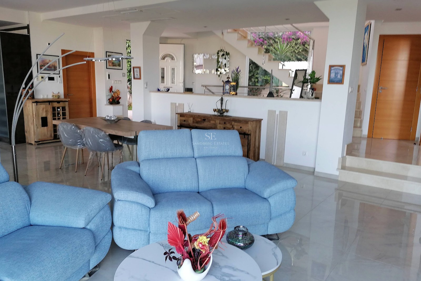 A spacious living room with blue sofas, polished marble floors, and an integrated dining area in a bright modern villa.