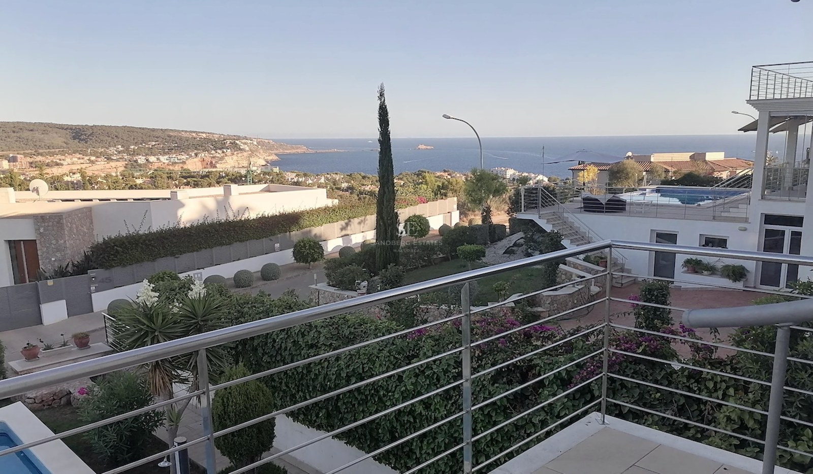 Elevated view from a terrace with stainless steel railings overlooking the Mediterranean Sea and coastal hills.