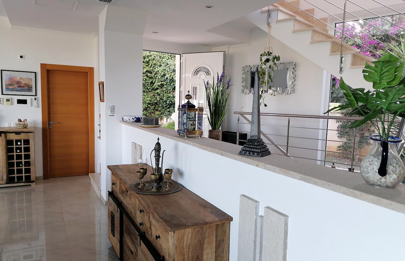 Spacious villa entrance featuring polished marble floors, a wooden sideboard, and an open staircase with steel railings.
