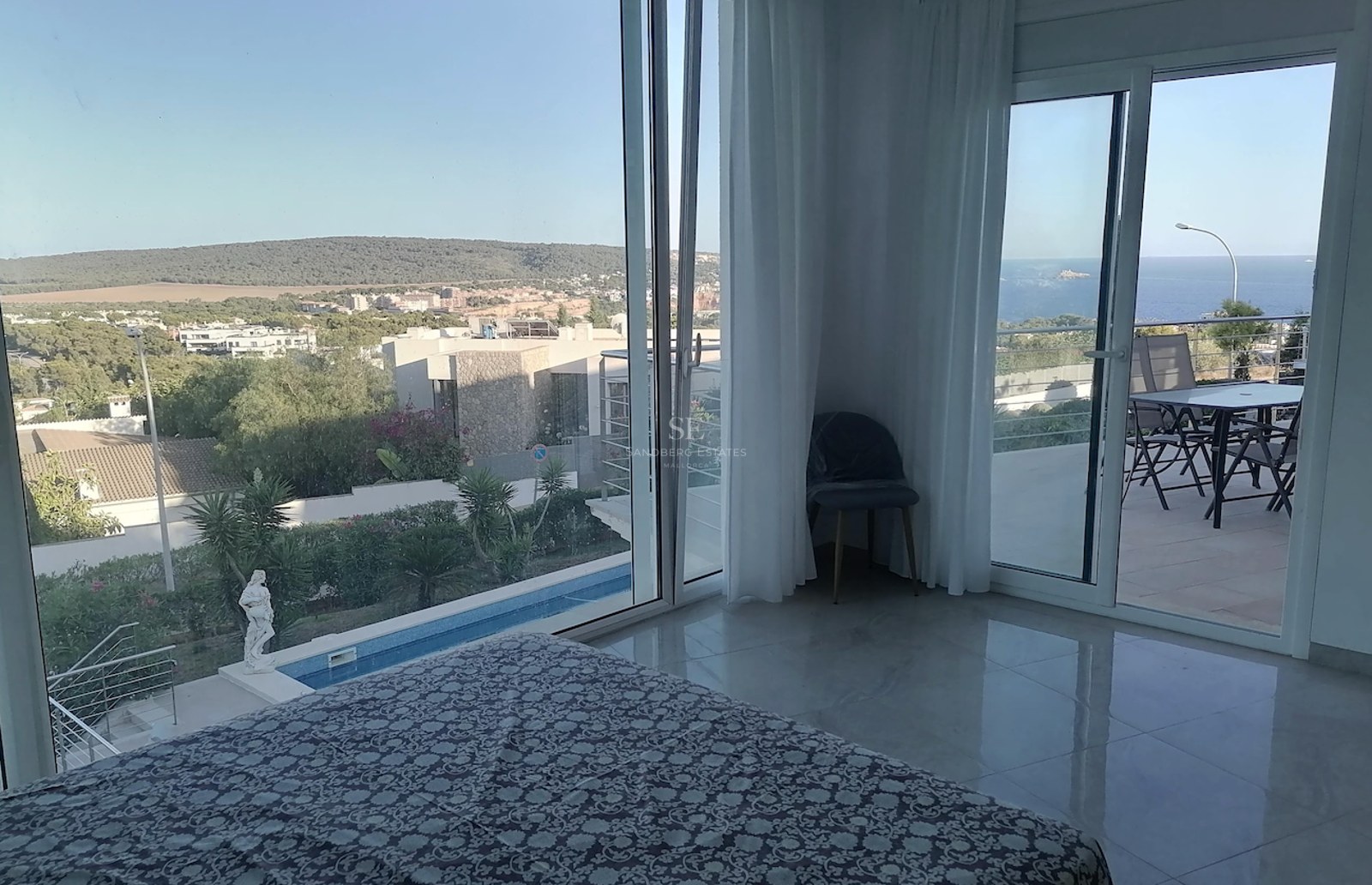 Master bedroom featuring polished marble floors and large glass doors opening to a private terrace overlooking the sea and pool.