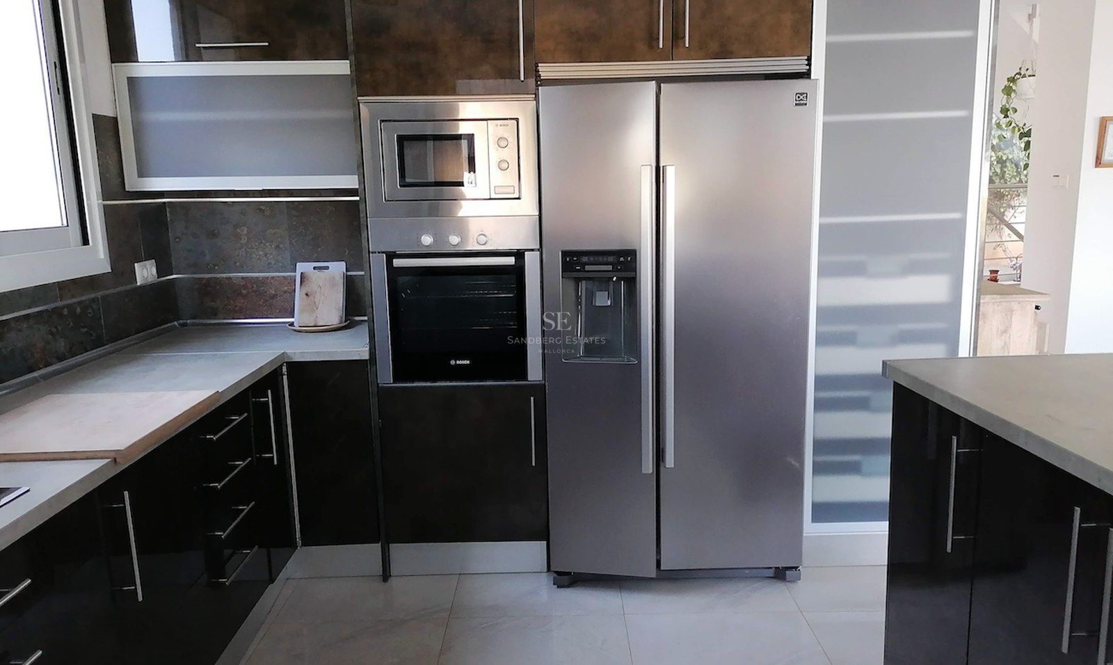 A contemporary kitchen featuring integrated Bosch appliances, a double-door stainless steel fridge, and dark gloss cabinets.