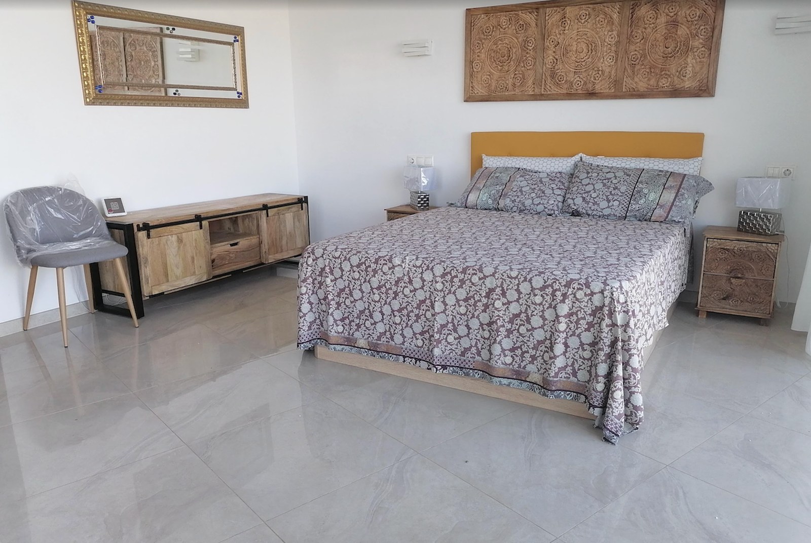 Bedroom featuring a double bed, carved wood headboard panel, polished tile flooring, and natural lighting.