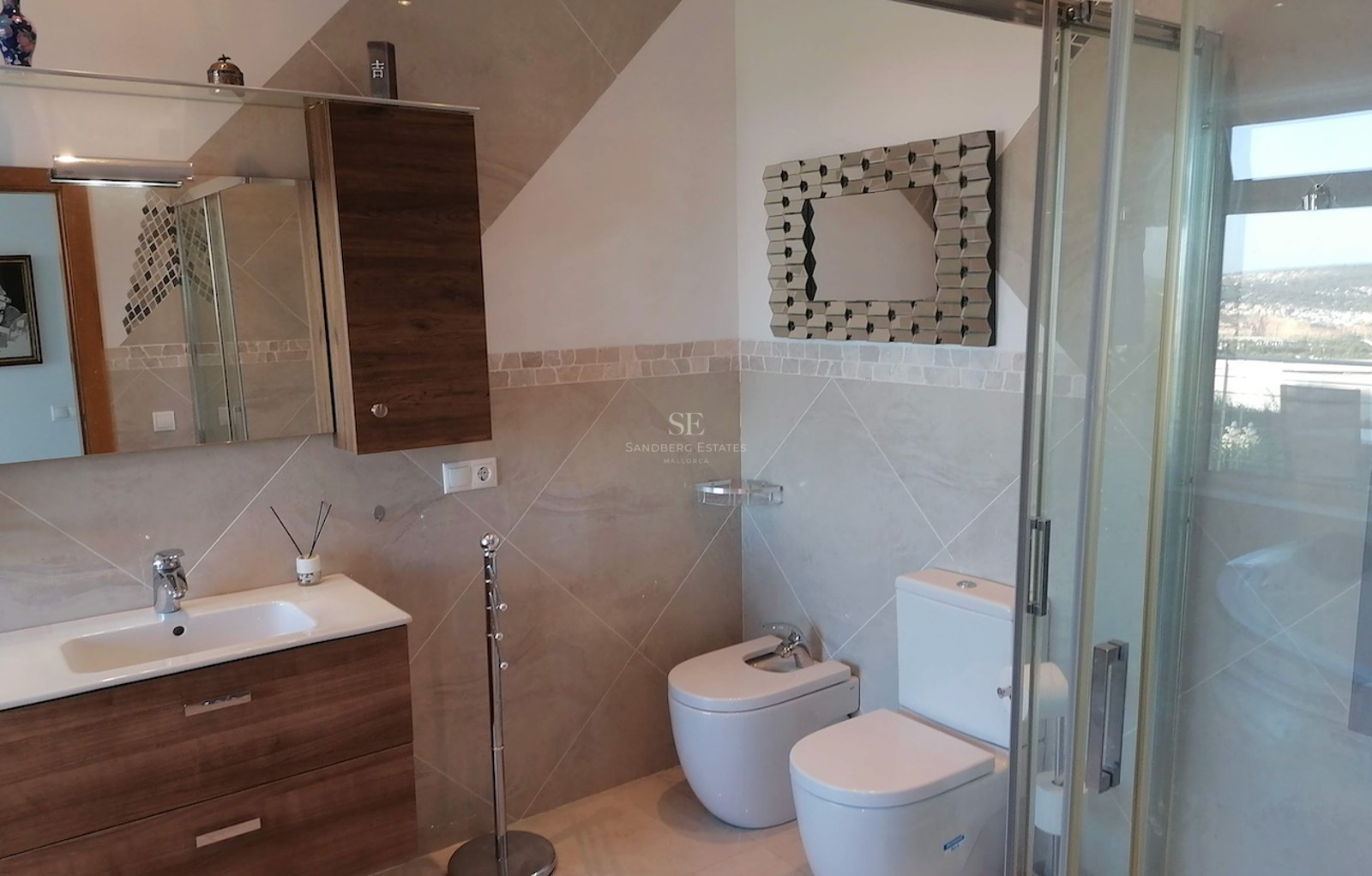 Modern bathroom featuring a wooden vanity, white ceramic toilet and bidet, and a glass-enclosed shower.