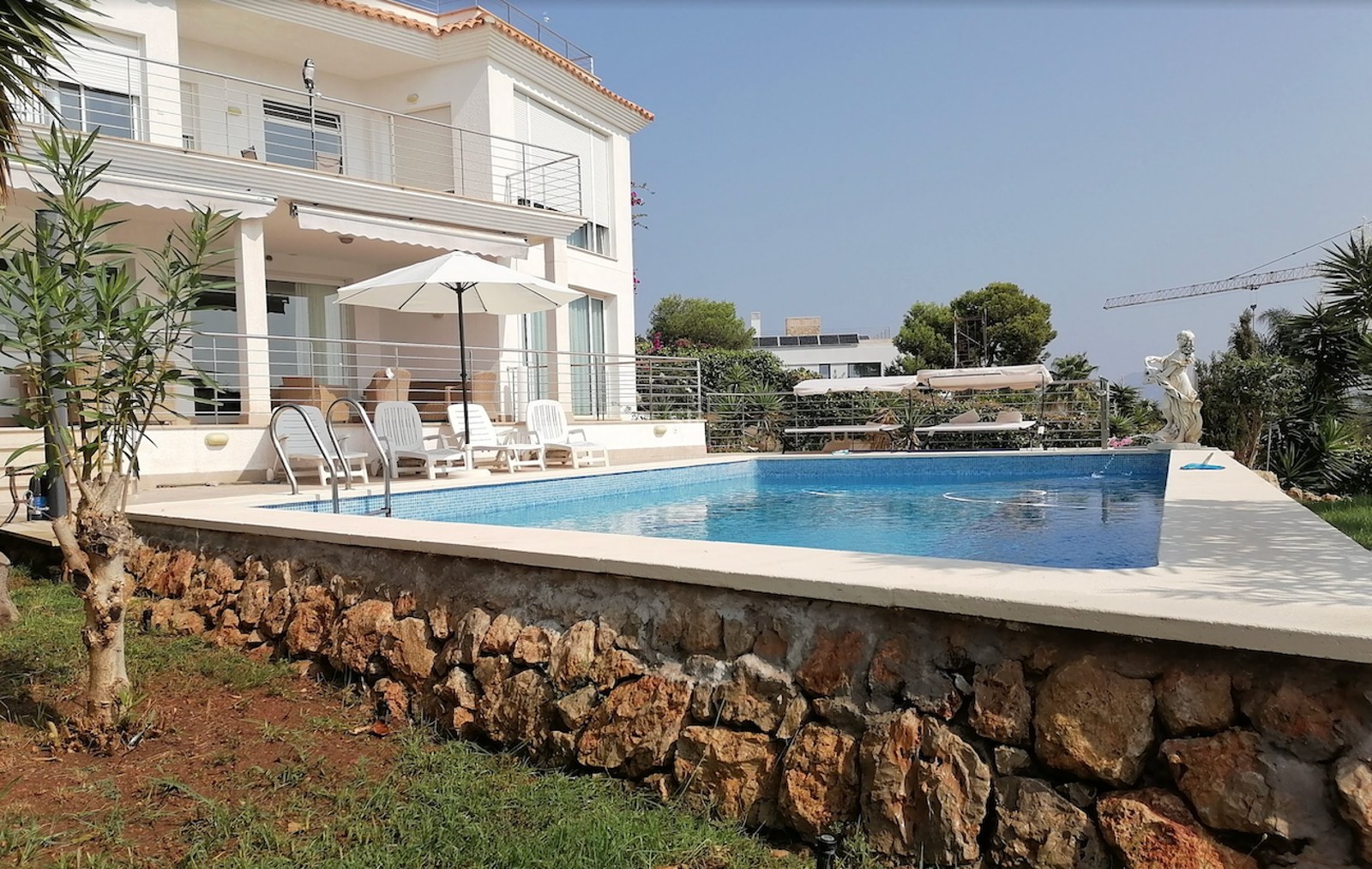 Private swimming pool with lounge chairs and stone retaining wall in front of a white Mediterranean villa.