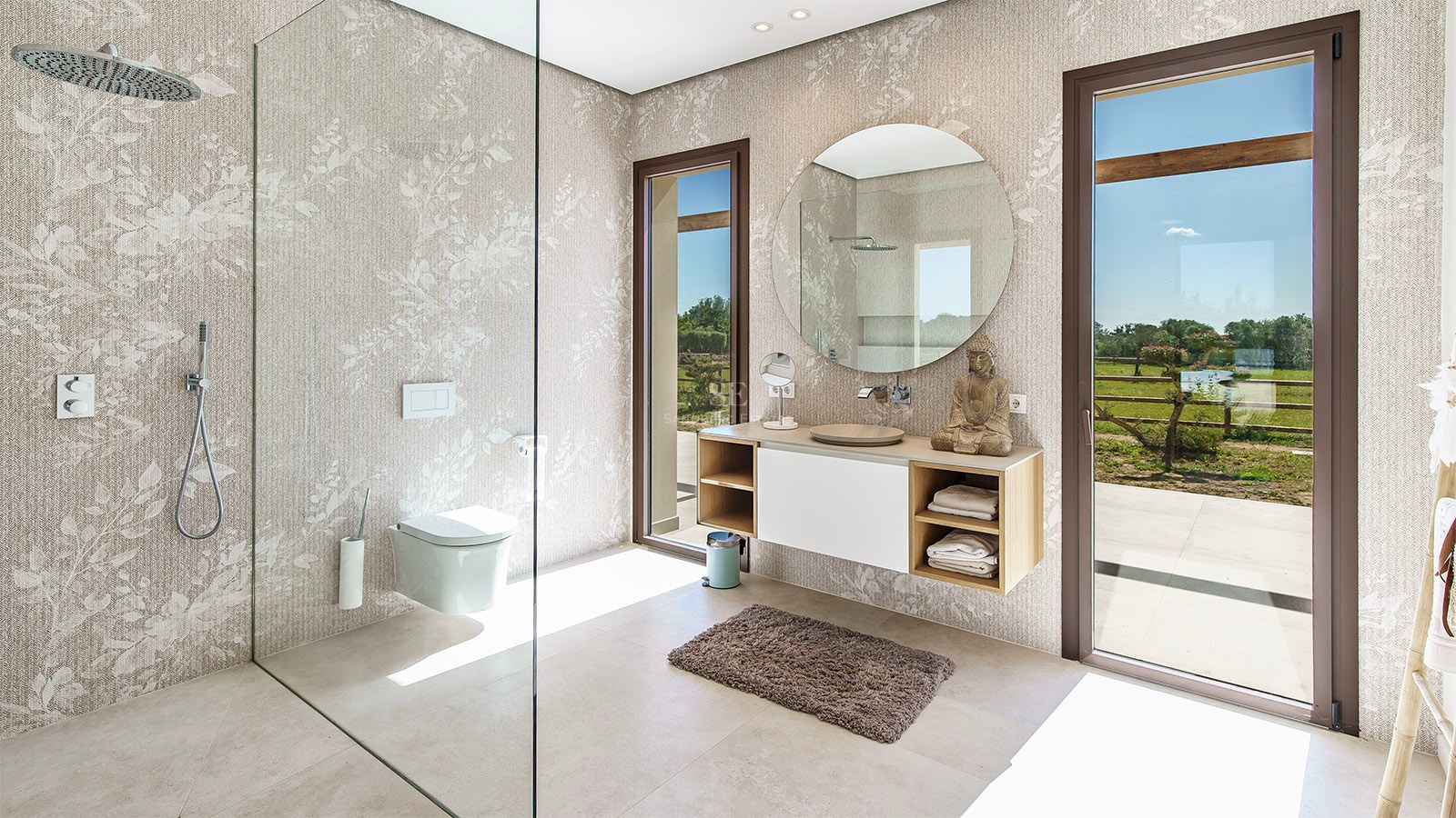Modern bathroom featuring a floating wooden vanity, circular mirror, and floor-to-ceiling windows overlooking a garden.