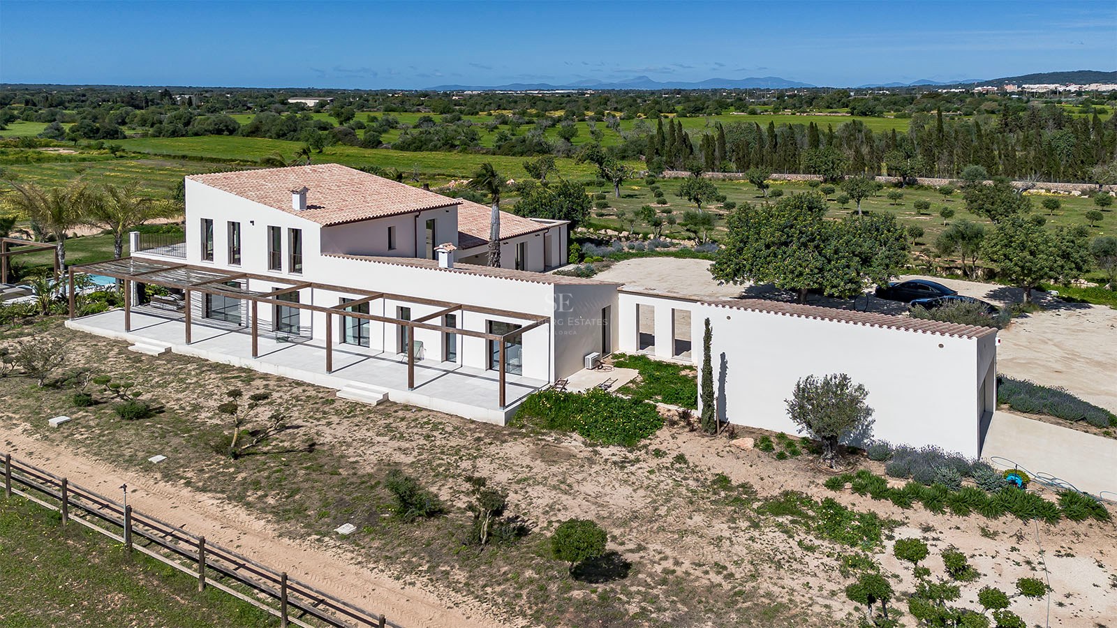 Aerial view of a white Mediterranean villa with wooden pergolas surrounded by lush green countryside.