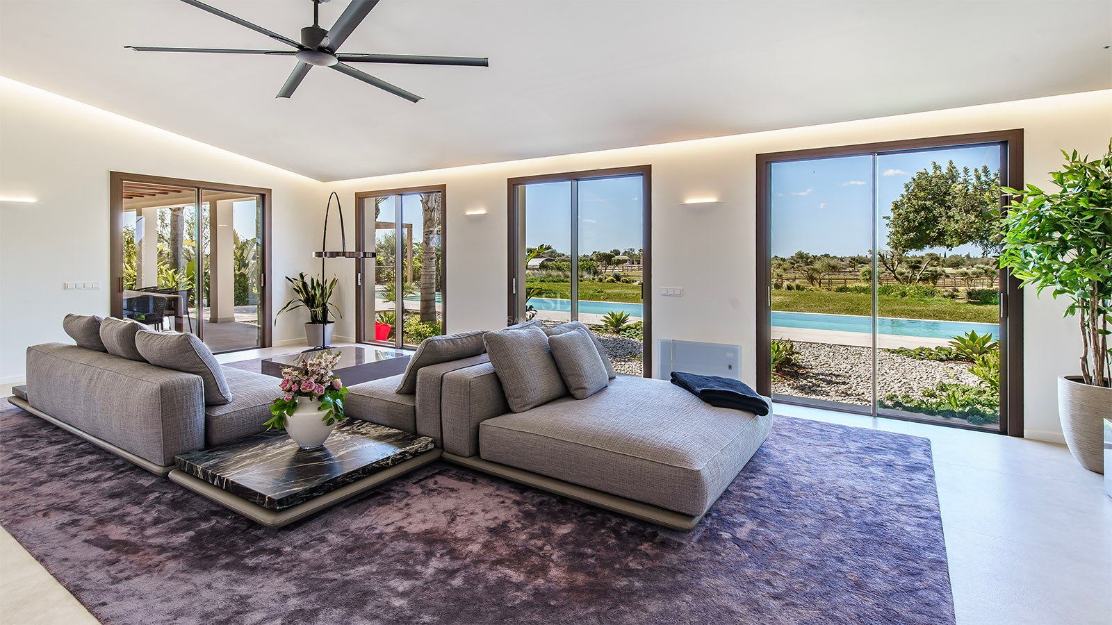 Contemporary living room featuring a modular grey sofa, marble coffee tables, and floor-to-ceiling garden views.