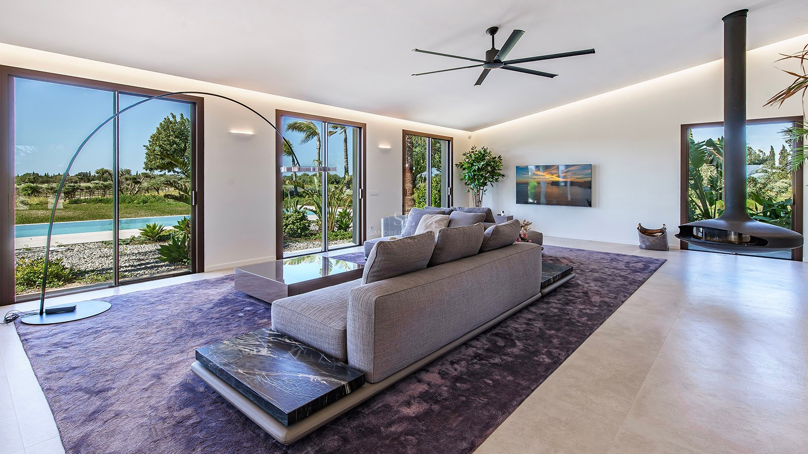 Modern living room featuring a grey sectional sofa on a purple rug with marble accents and large garden-facing windows.