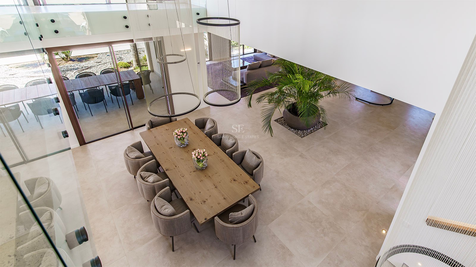 High-angle view of a modern dining room featuring a solid wood table, grey upholstered chairs, and ring pendant lights.