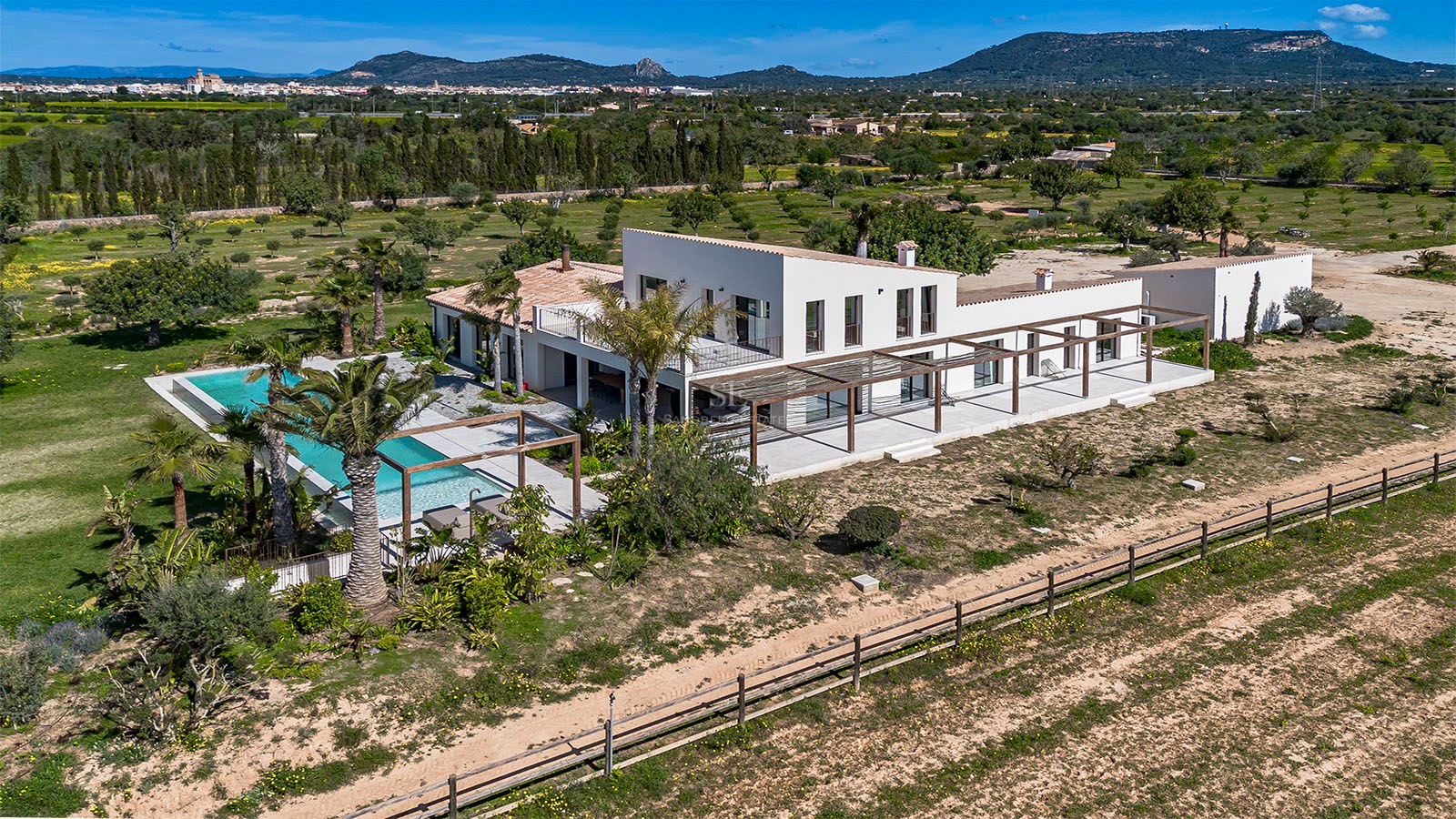Elevated view of a white contemporary villa with a swimming pool, wooden pergolas, and mountain backdrop.