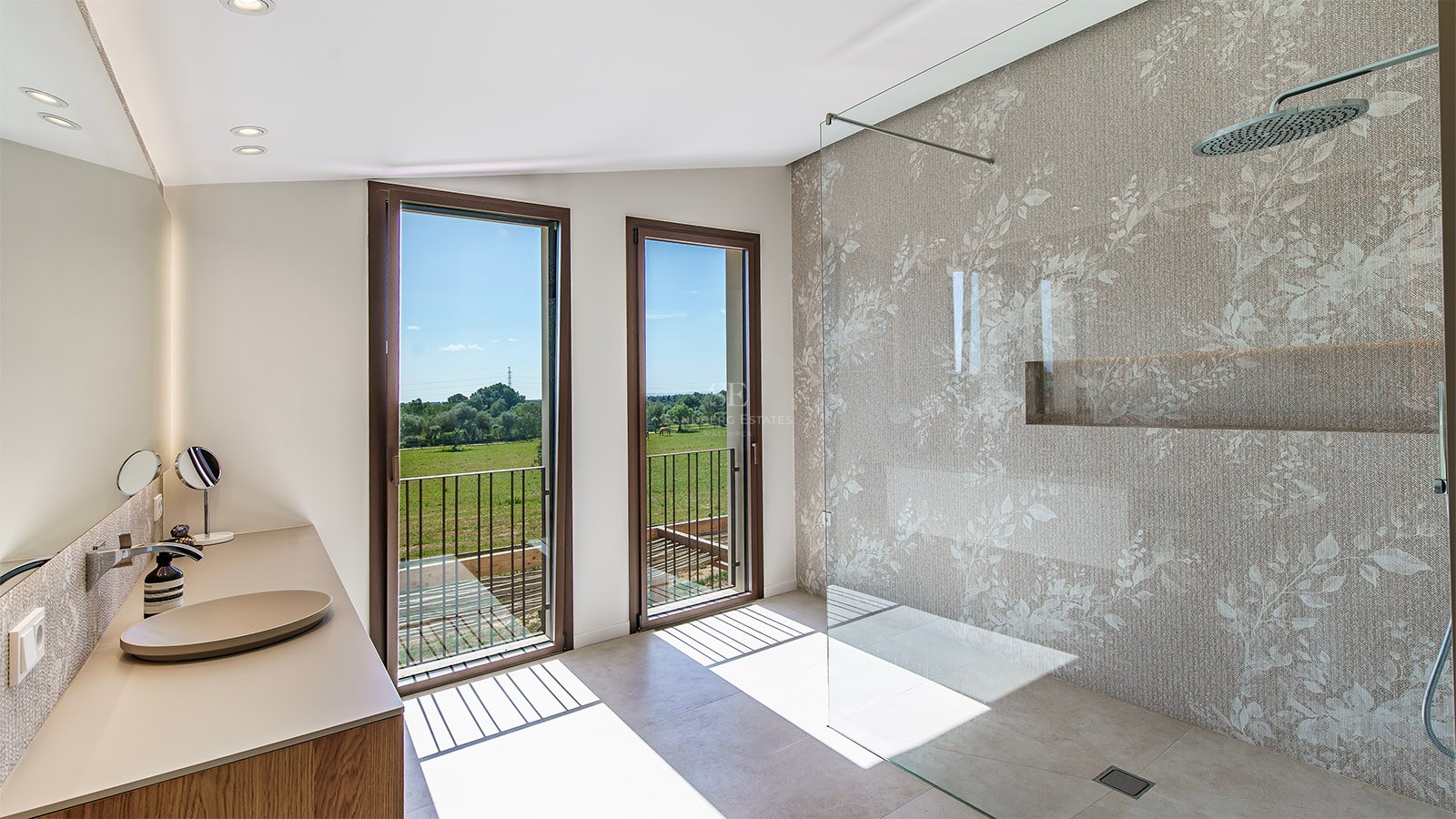 A minimalist bathroom featuring a glass walk-in shower and tall windows overlooking a lush green landscape.