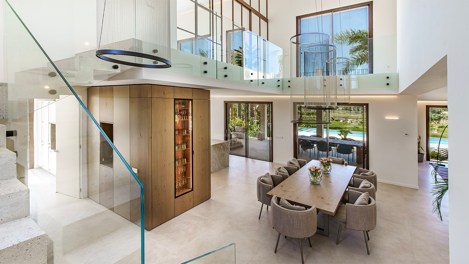 Double-height dining room featuring a wooden table, glass mezzanine gallery, and integrated wine display.
