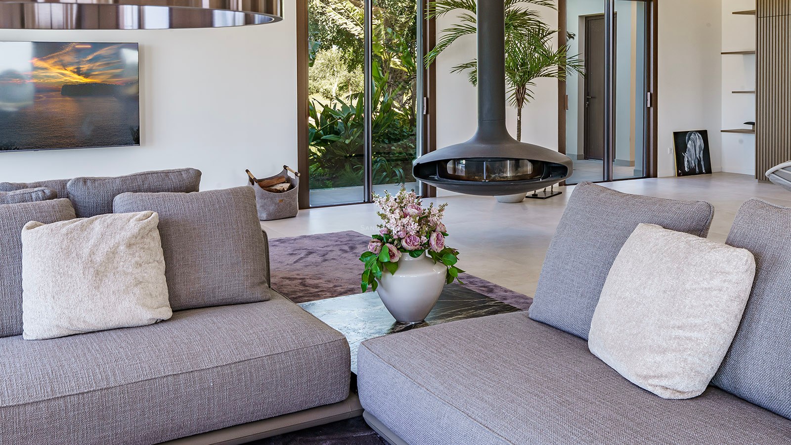 Close-up of a modern living room featuring a black suspended fireplace, grey sofas, and garden views through glass doors.