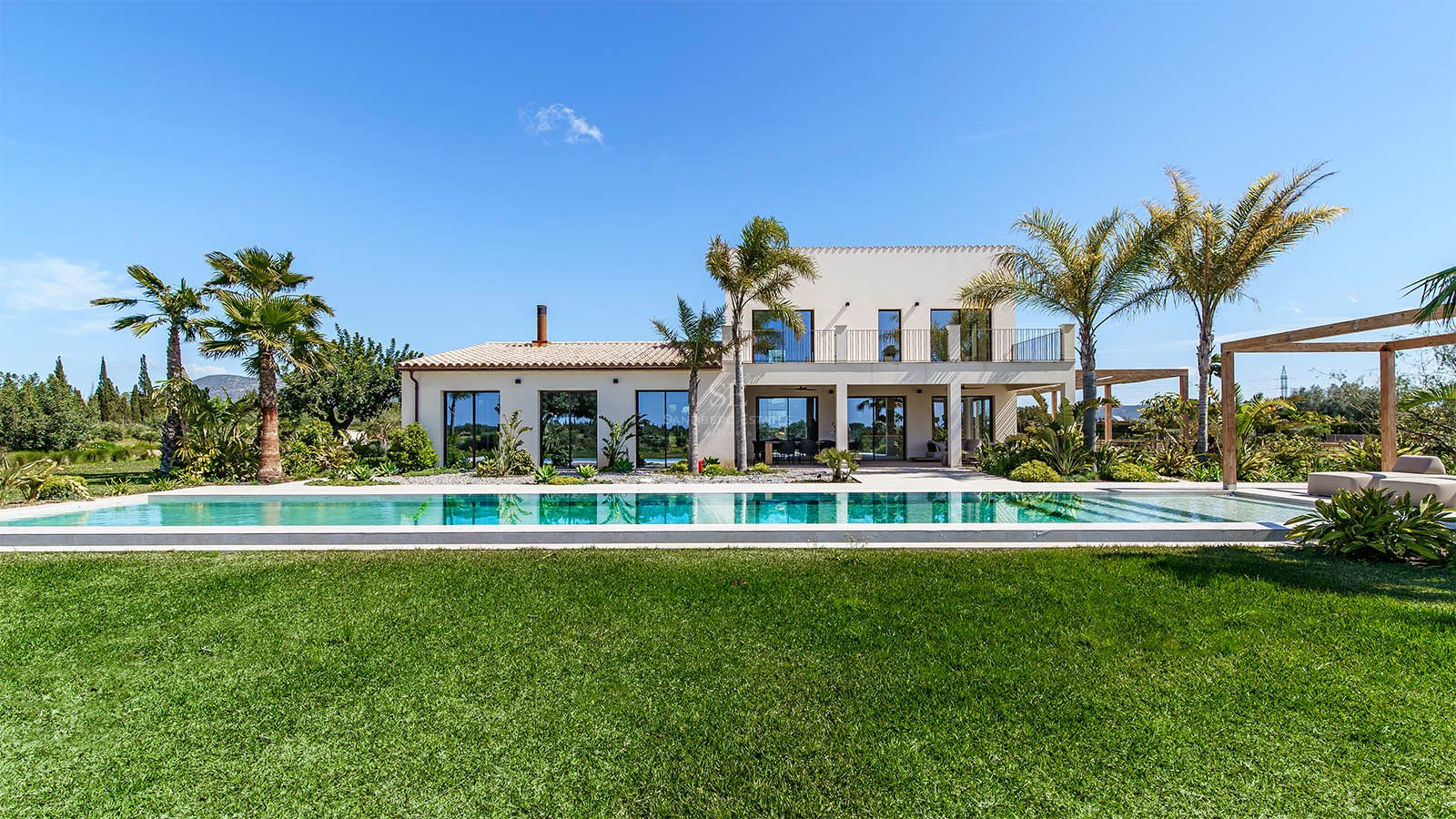 Exterior view of a modern two-story white villa with a large rectangular swimming pool and green lawn under a clear sky.