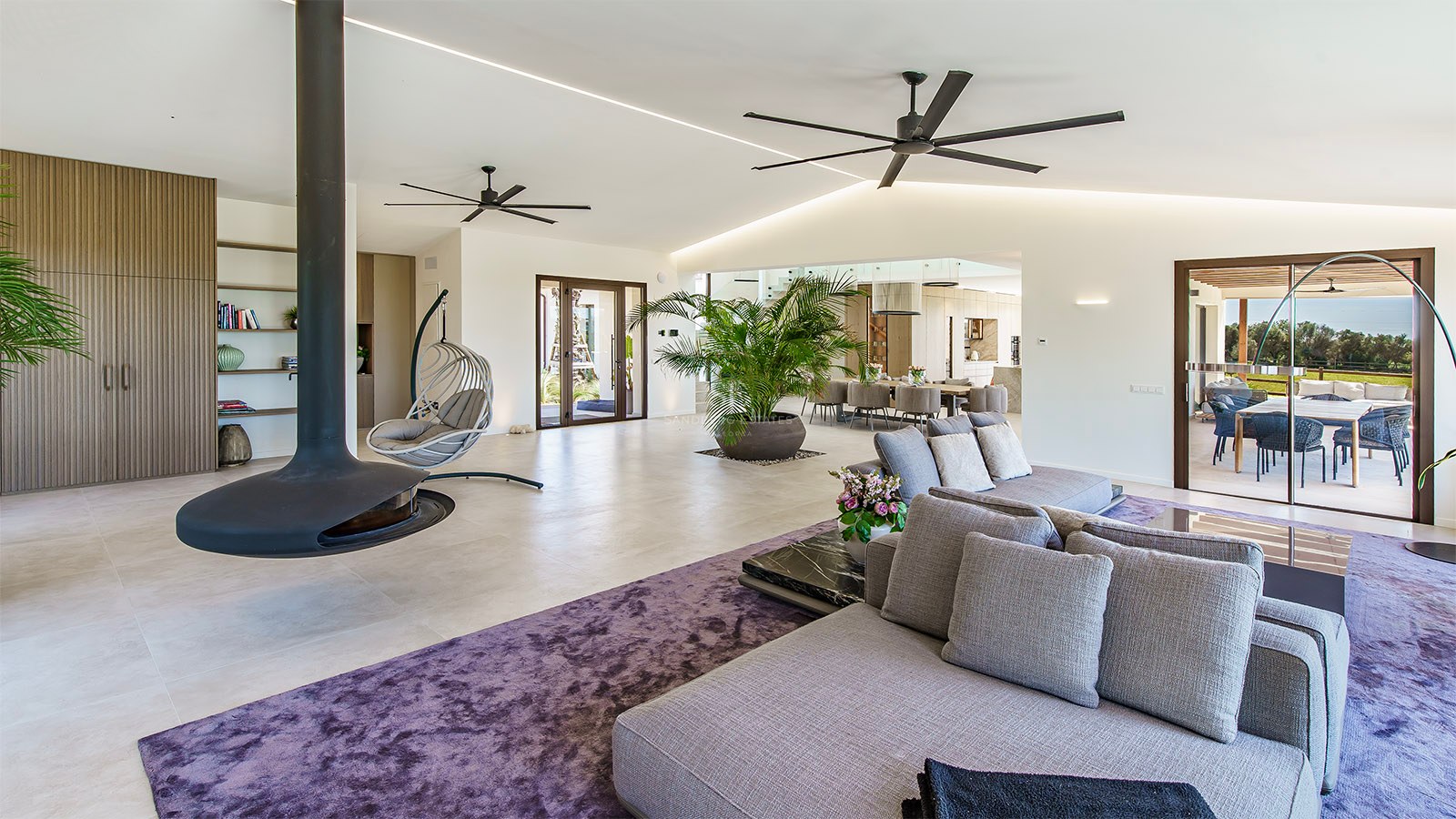 A contemporary living room featuring a large gray sofa, a purple textured rug, and dual industrial ceiling fans.