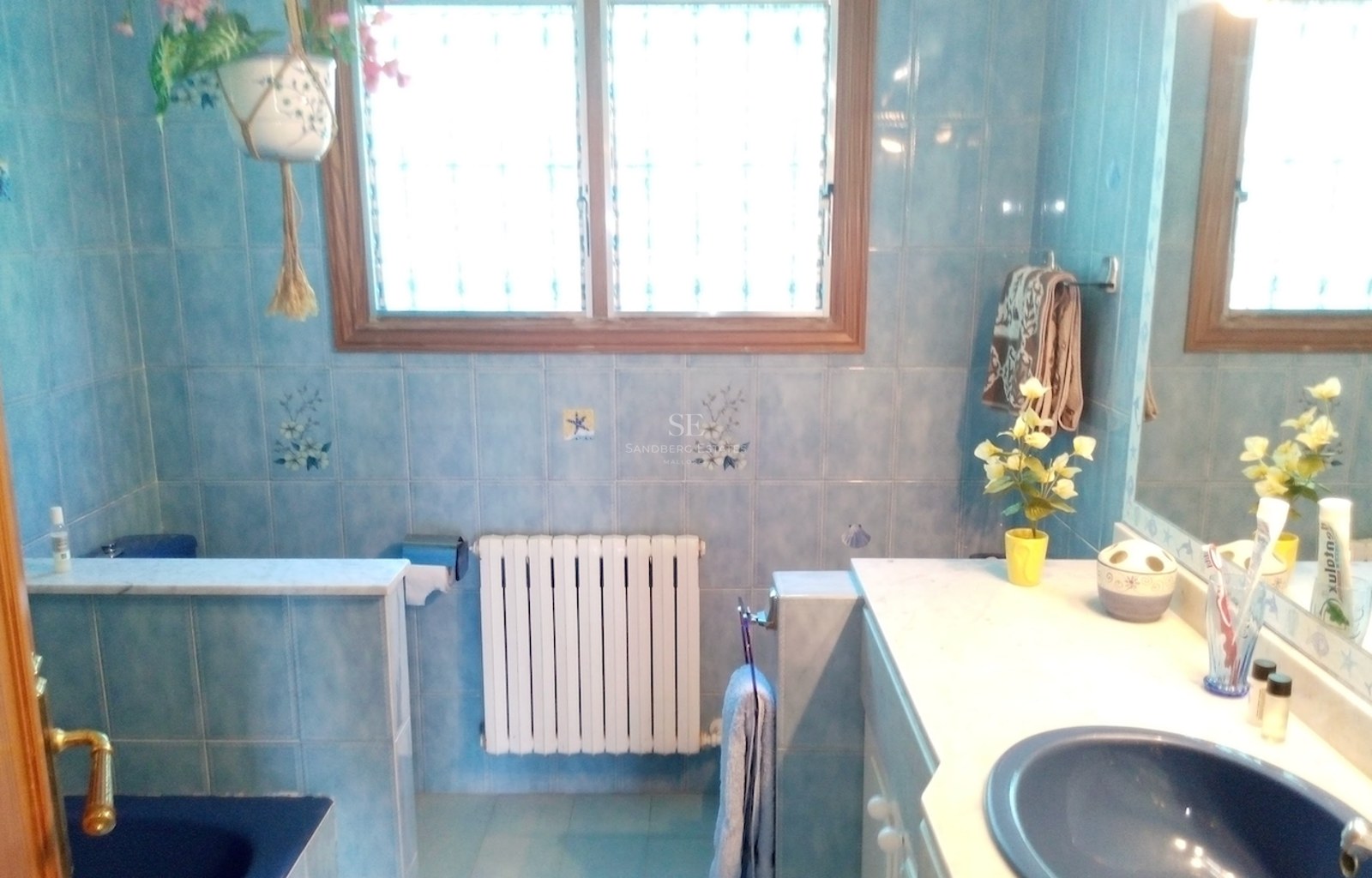 Salle de bain avec carrelage bleu à motifs, plan de toilette en marbre blanc et grande fenêtre.