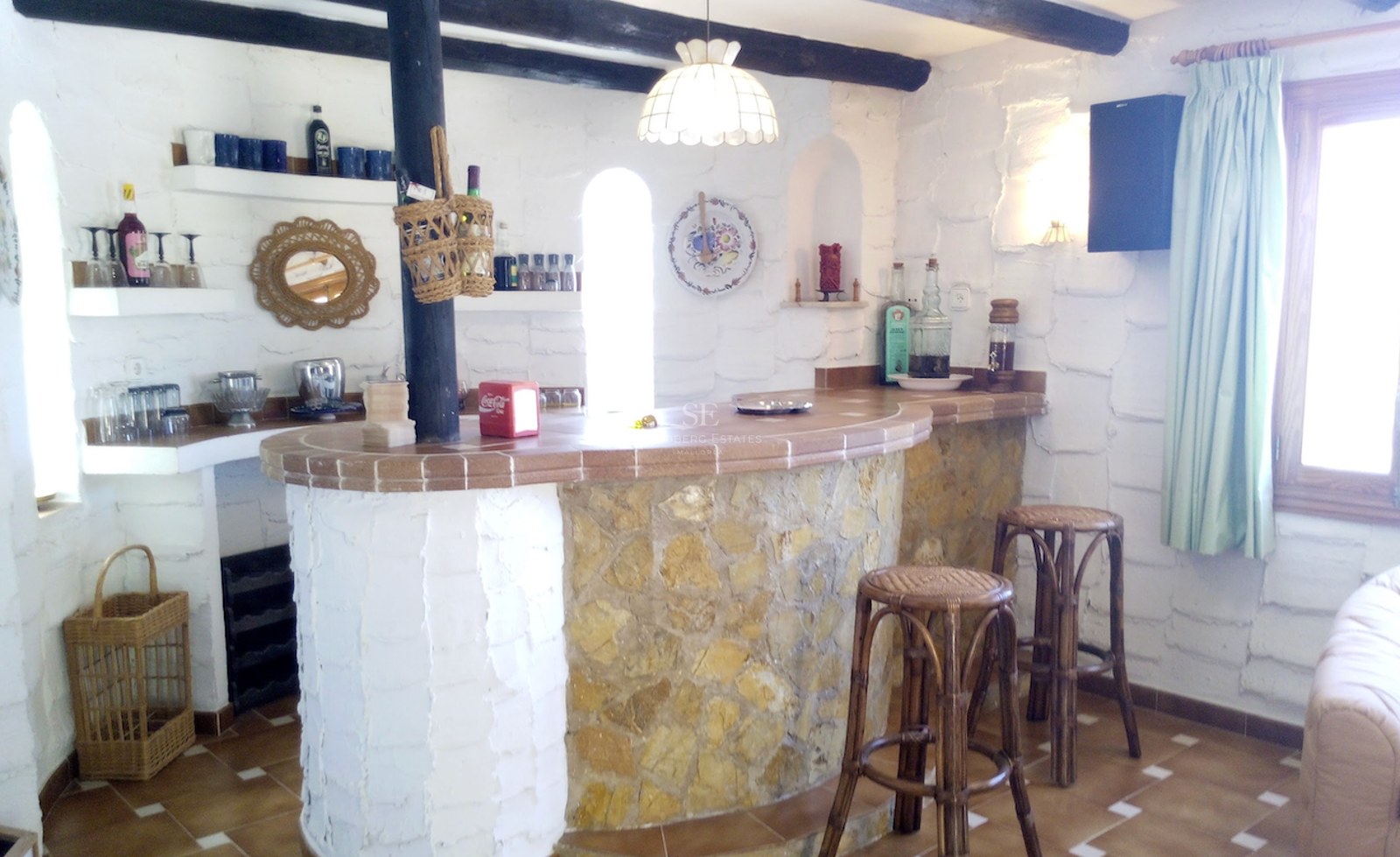 Un bar intérieur avec une base en pierre courbée, un comptoir en terre cuite et des poutres en bois sombre au plafond.