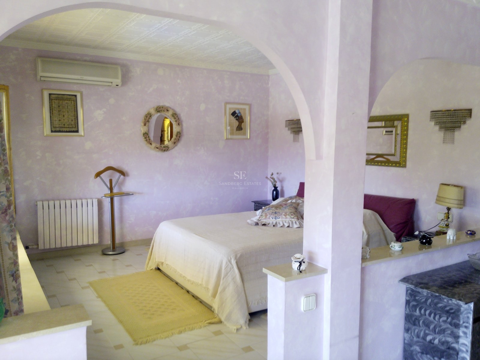 Chambre avec murs texturés lilas, arches décoratives, lit double et sol en carrelage clair.