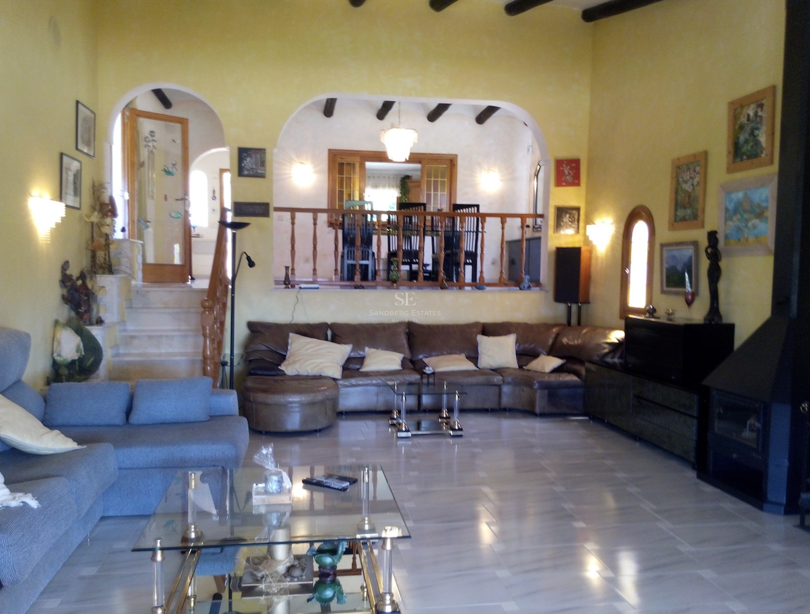 Grand salon avec sols en marbre poli, plafonds à poutres apparentes, arches décoratives et coin repas surélevé.