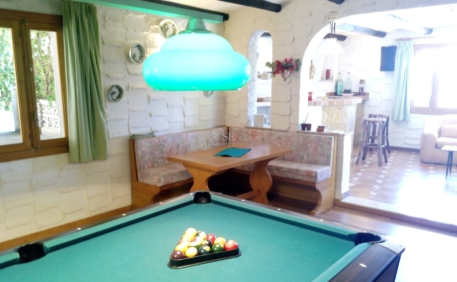 Une salle de jeux rustique comprenant un billard, un coin salon en bois et des murs en pierre blanche.