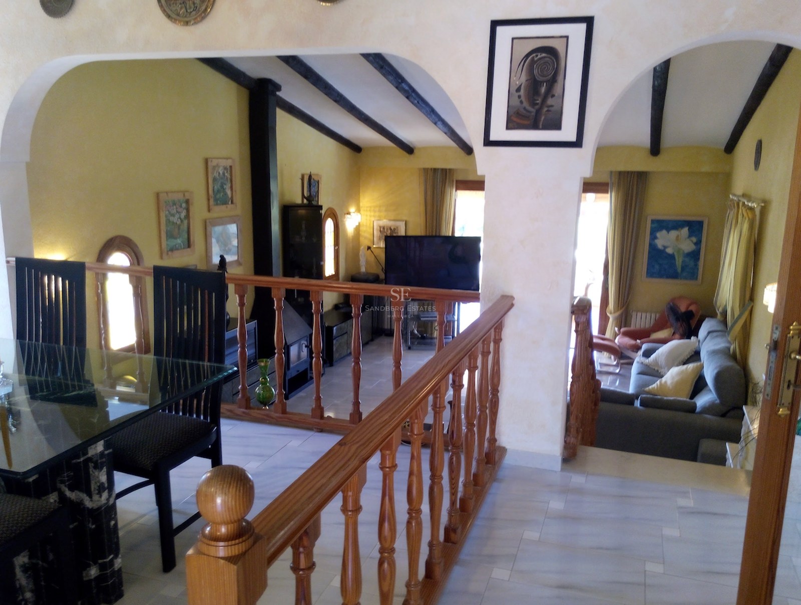 Salon en duplex avec sol en marbre, balustrade en bois et poutres sombres sous des arches blanches.