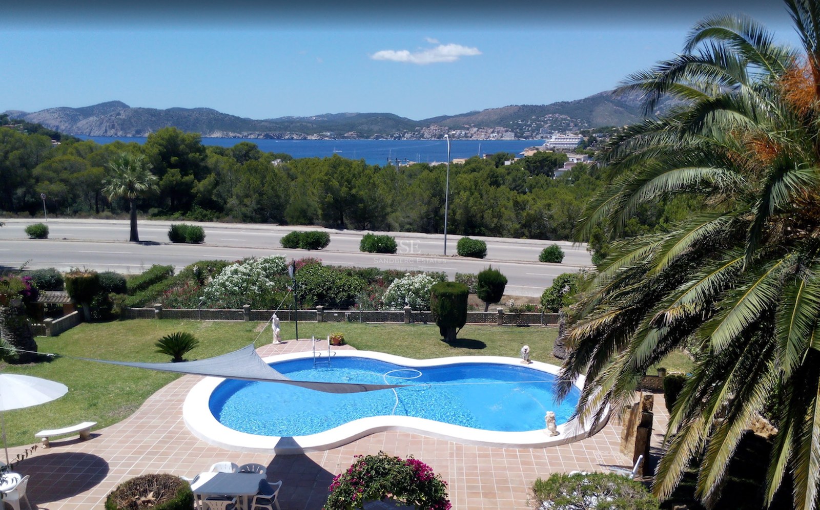 Piscine en forme de haricot entourée de terre cuite et d'un jardin avec vue sur la Méditerranée et les montagnes.