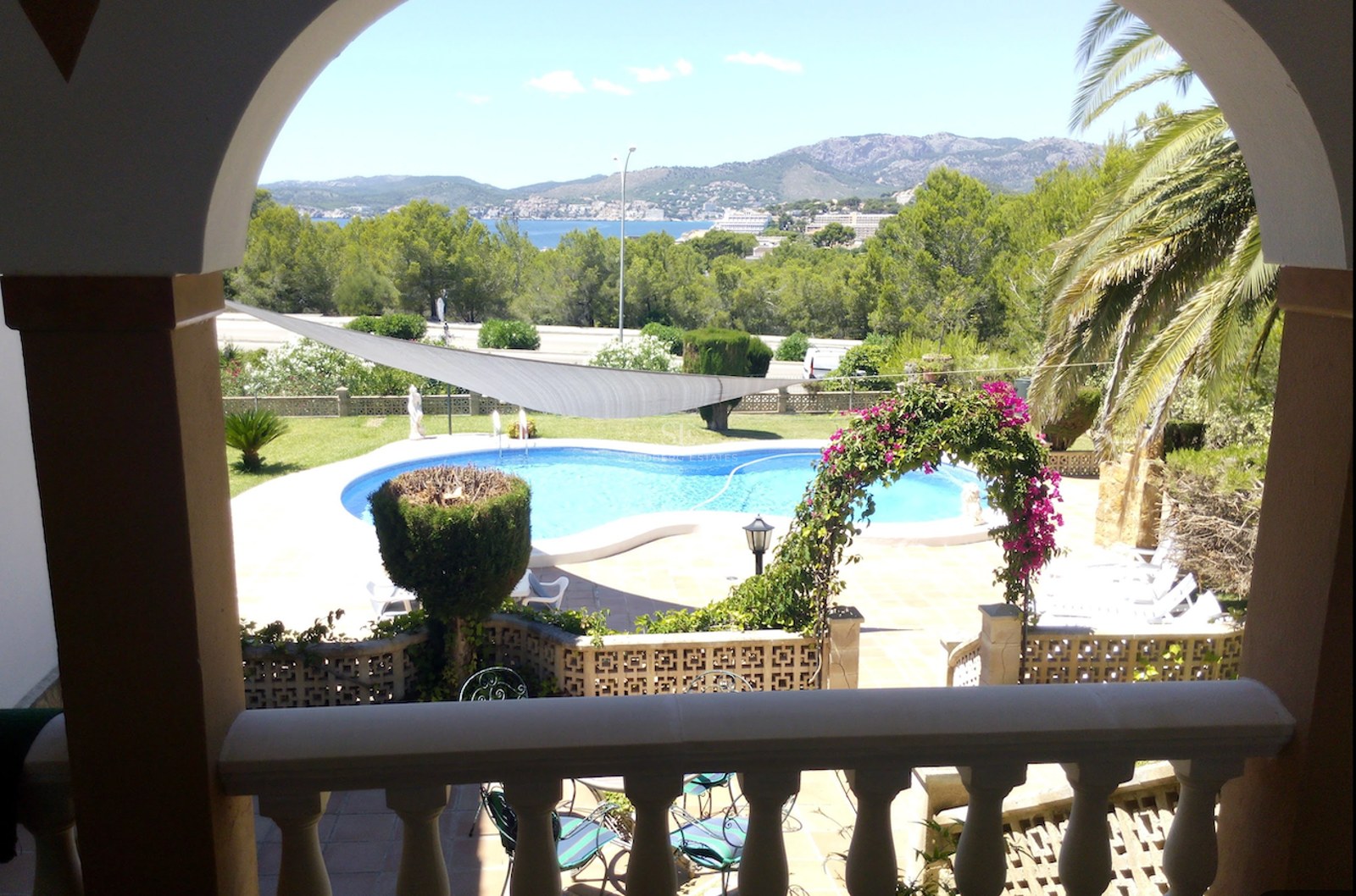 Vue à travers une arche d'une piscine turquoise, d'un jardin luxuriant et de la mer Méditerranée au loin.