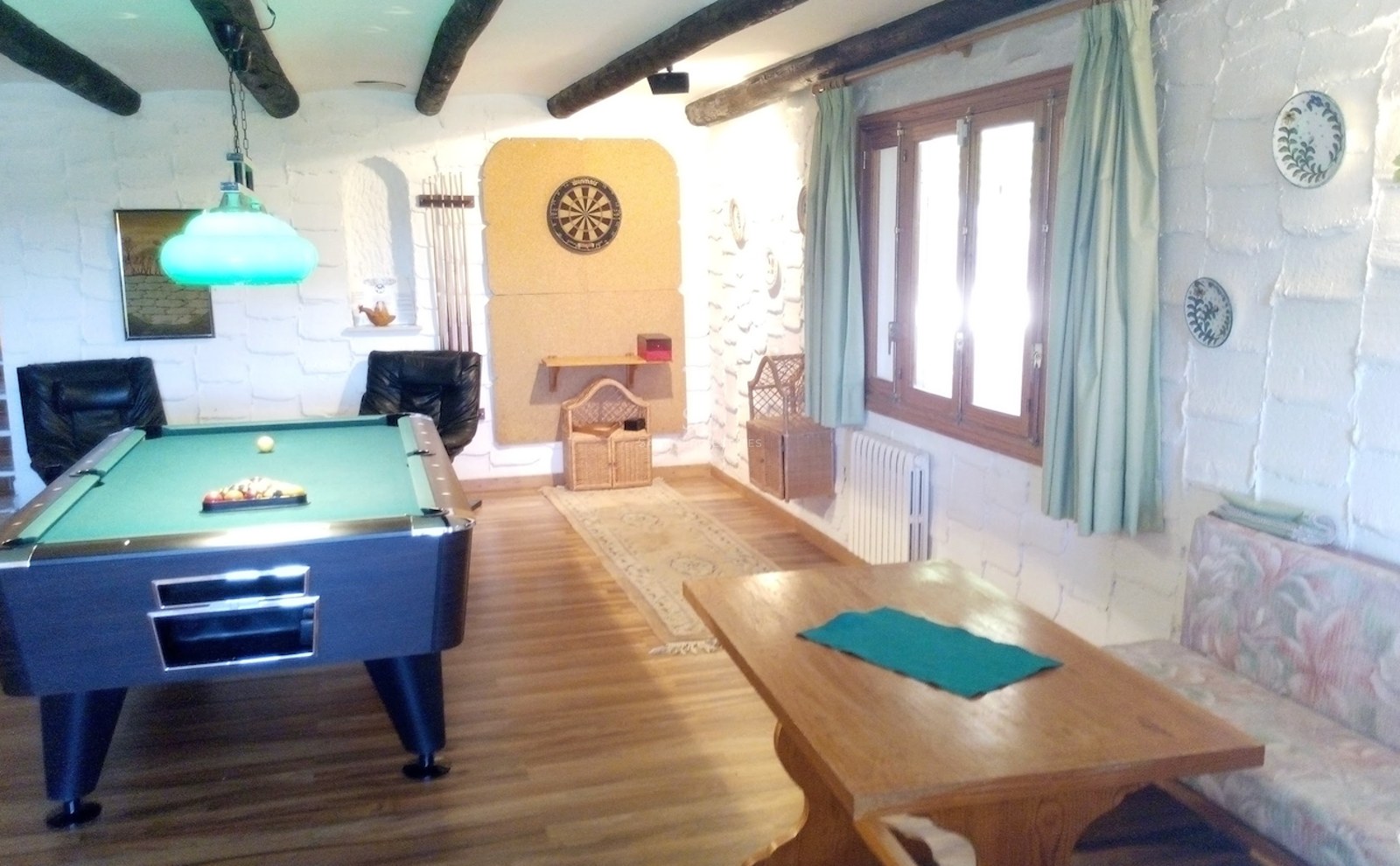 Salle de loisirs avec table de billard, jeu de fléchettes, murs en pierre blanche et poutres en bois sombre.