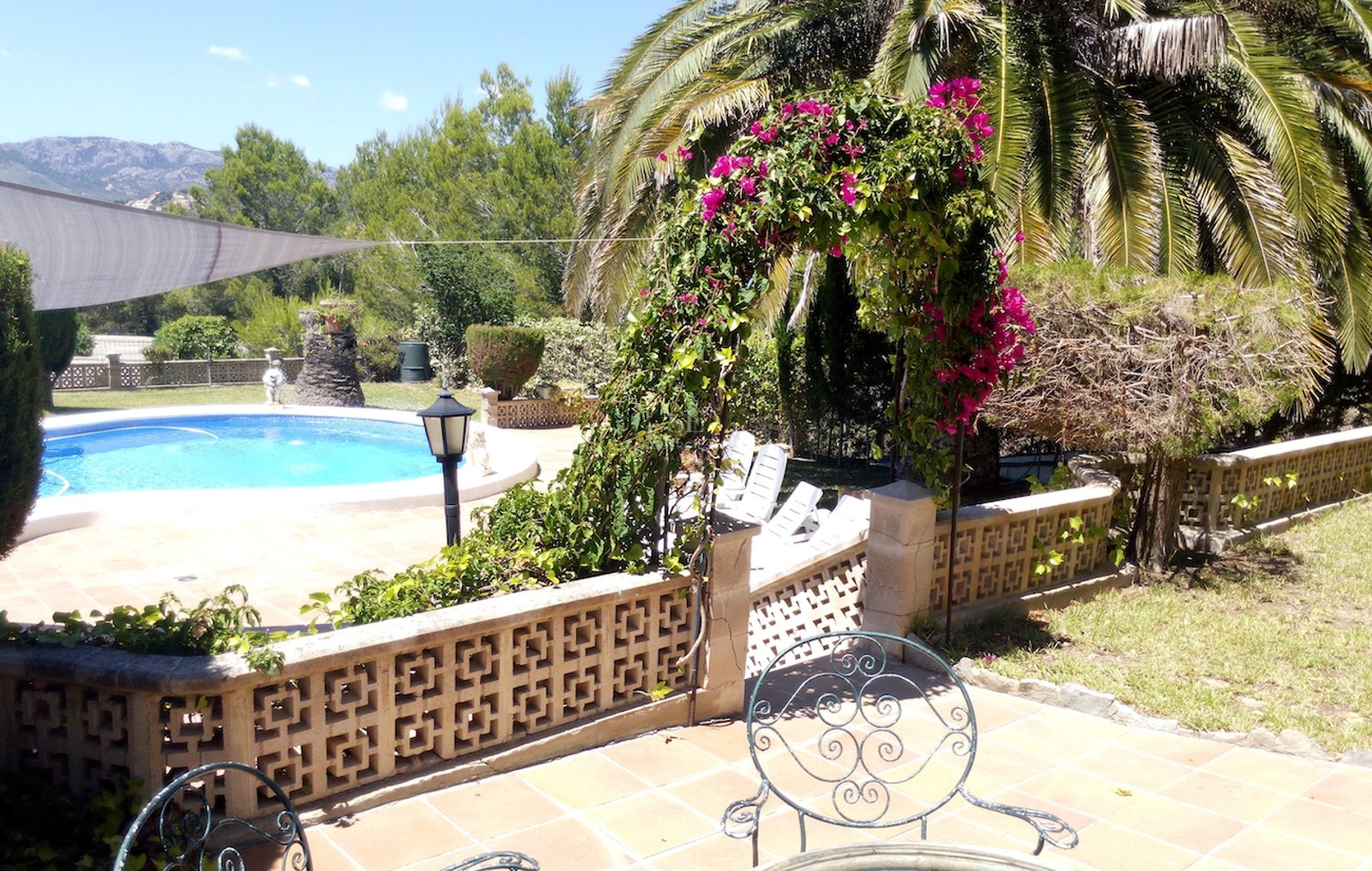 Terrasse ensoleillée avec piscine circulaire, carrelage en terre cuite, arche de bougainvilliers et montagnes au loin.