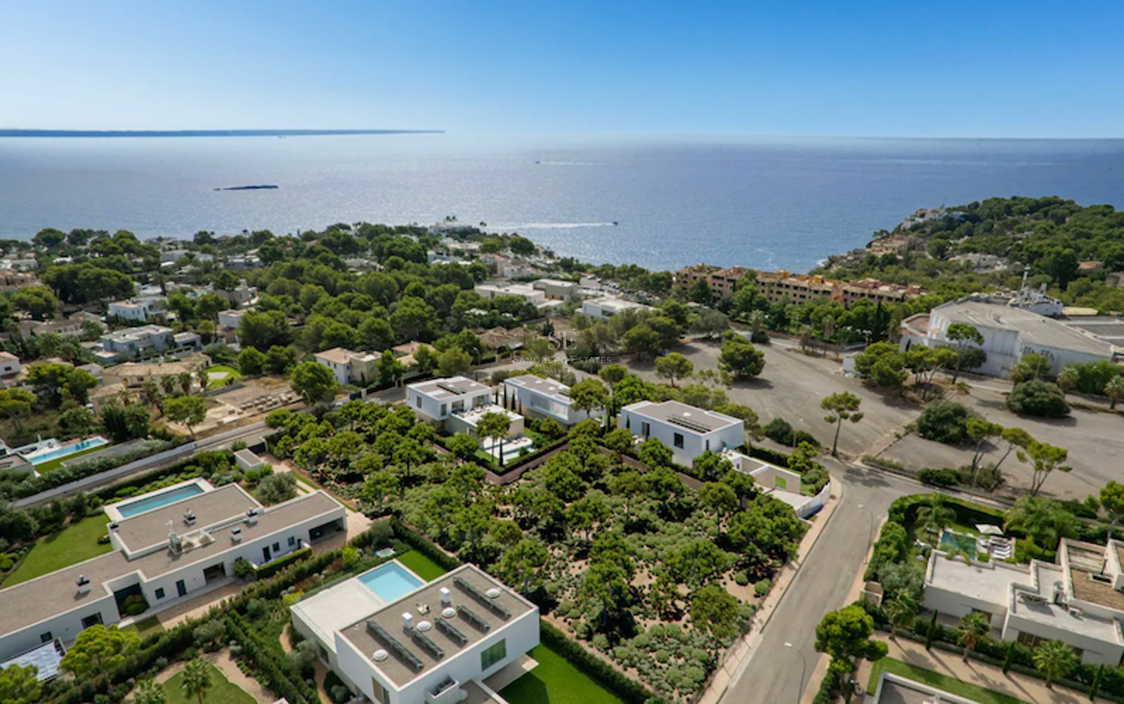 Luftaufnahme moderner weißer Villen in einer grünen Küstenlandschaft mit Blick auf das blaue Mittelmeer.