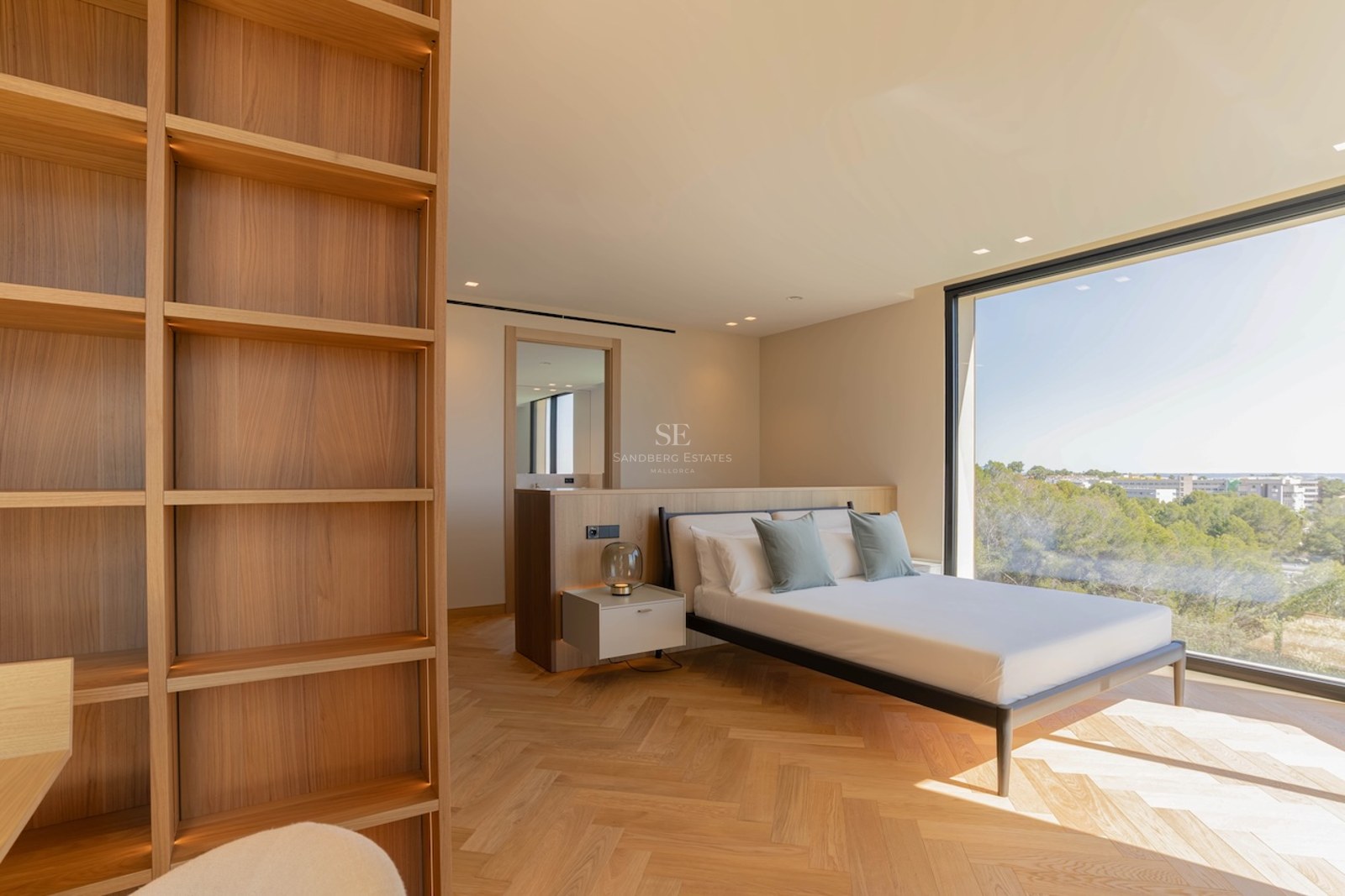 Chambre contemporaine avec parquet en chêne, bibliothèque intégrée et grande baie vitrée donnant sur la nature.
