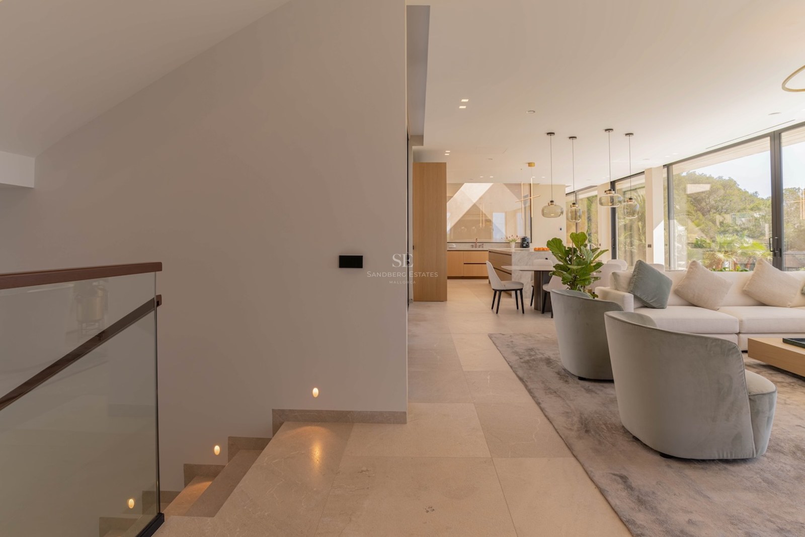 Vue d'un salon moderne à aire ouverte depuis un escalier en pierre avec garde-corps en verre et grandes baies vitrées.