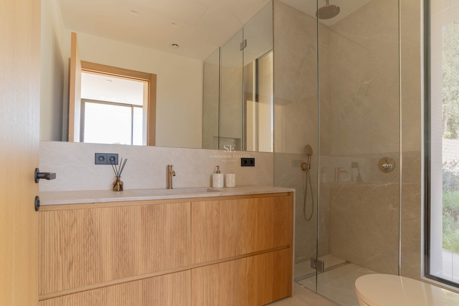 Salle de bain moderne avec meuble en bois clair, plan de travail en pierre, grand miroir et douche vitrée.