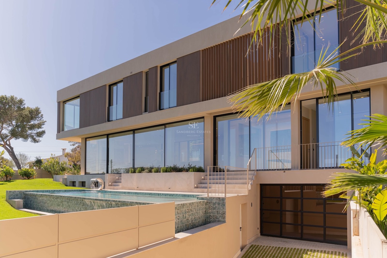 Façade d'une villa moderne de deux étages avec de grandes baies vitrées, piscine à débordement et persiennes en bois.