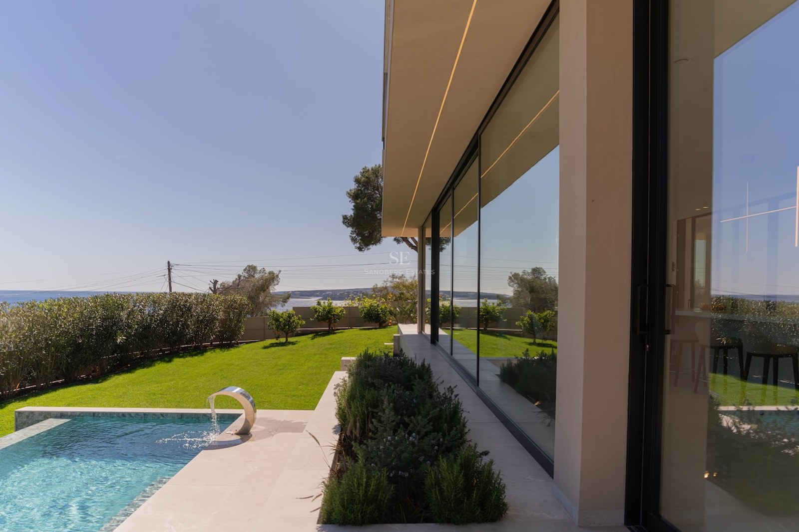 Extérieur d'une villa moderne avec piscine turquoise, pelouse verdoyante et grandes baies vitrées.